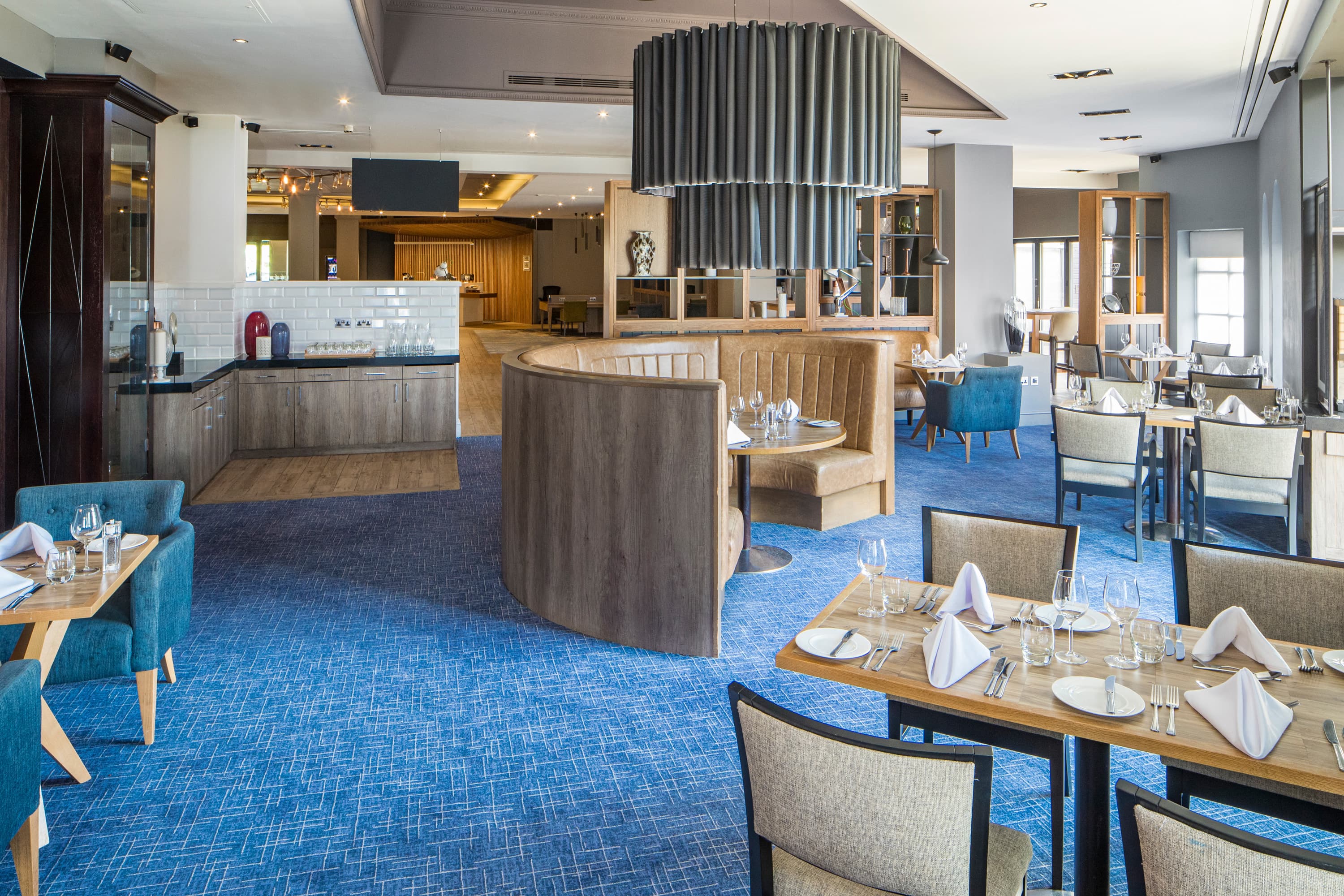 Terrace restaurant with blue carpet, curved booth seating and laid dining tables.