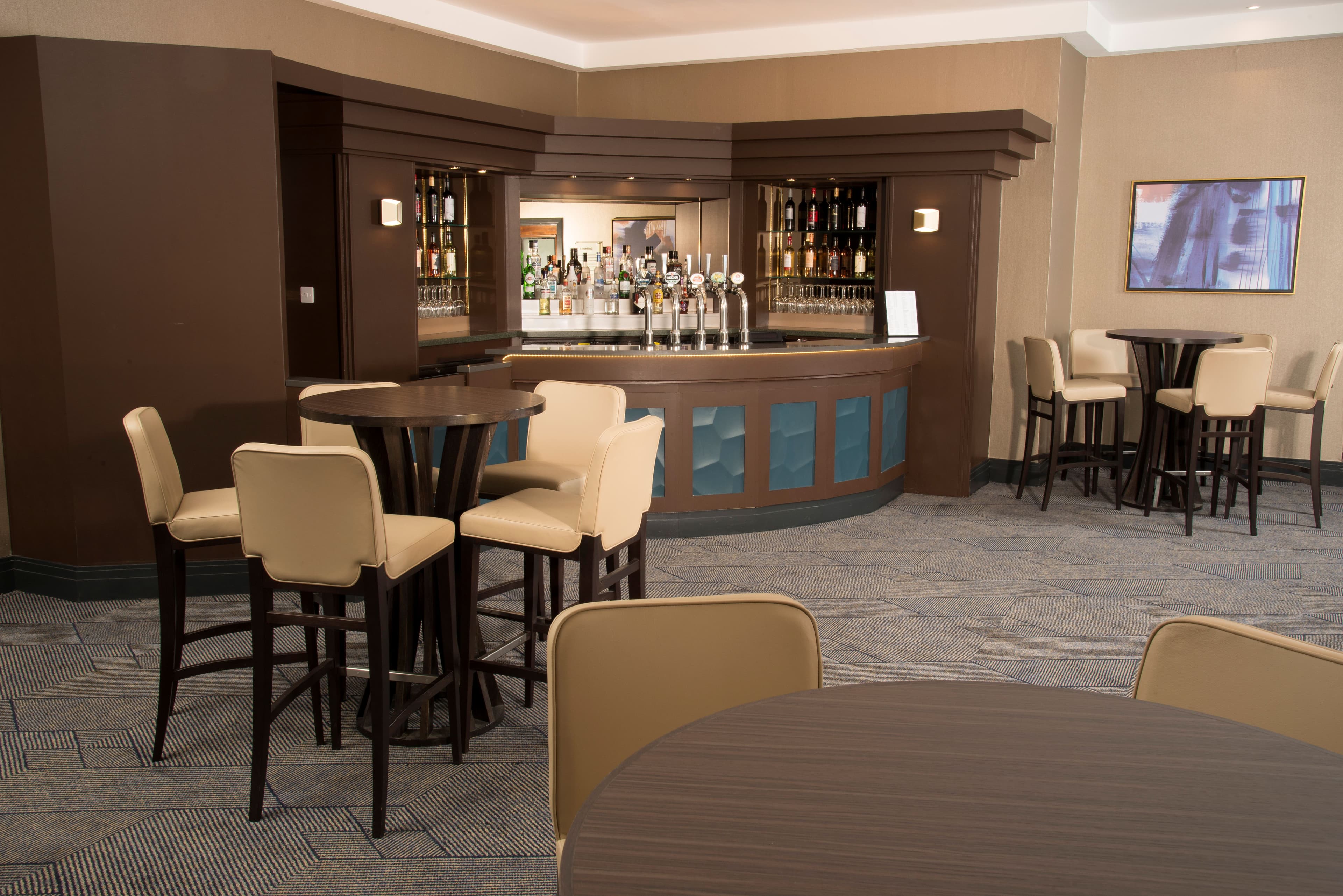 Hotel bar area with curved counter, draught taps, high stools and patterned carpet.