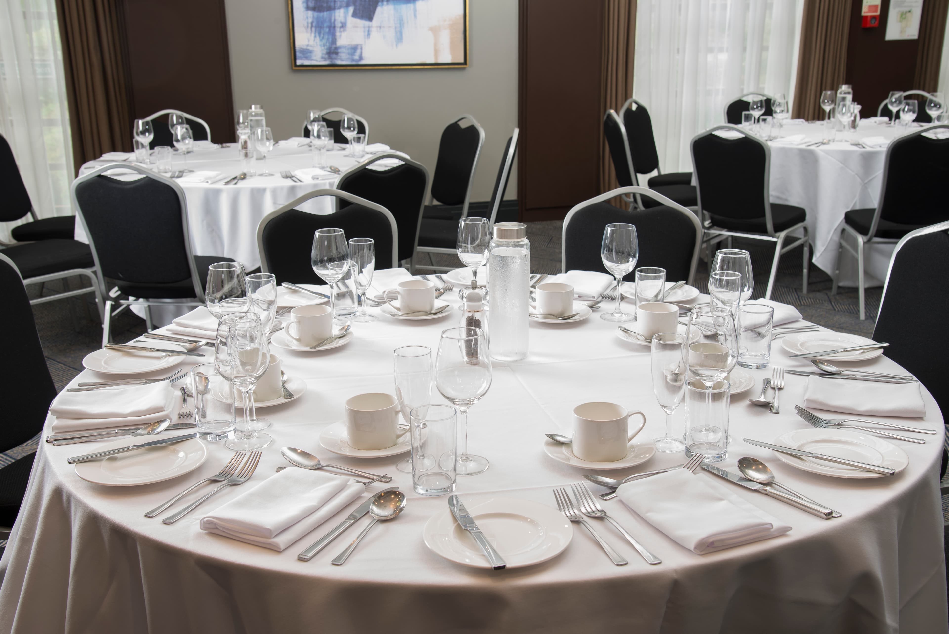 Formally laid round tables with white linen, glassware and cutlery in a function room.