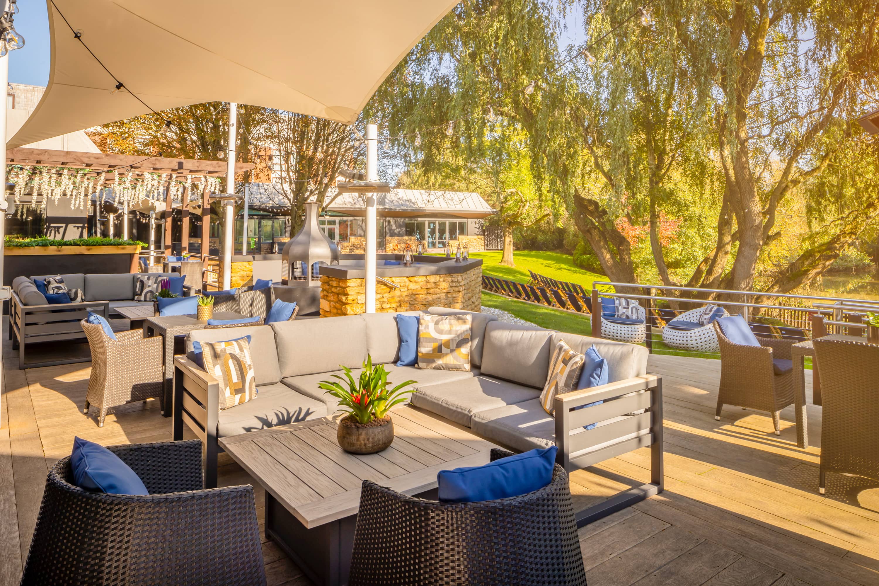 Sunny outdoor terrace with rattan seating, blue cushions and views over lawned gardens.