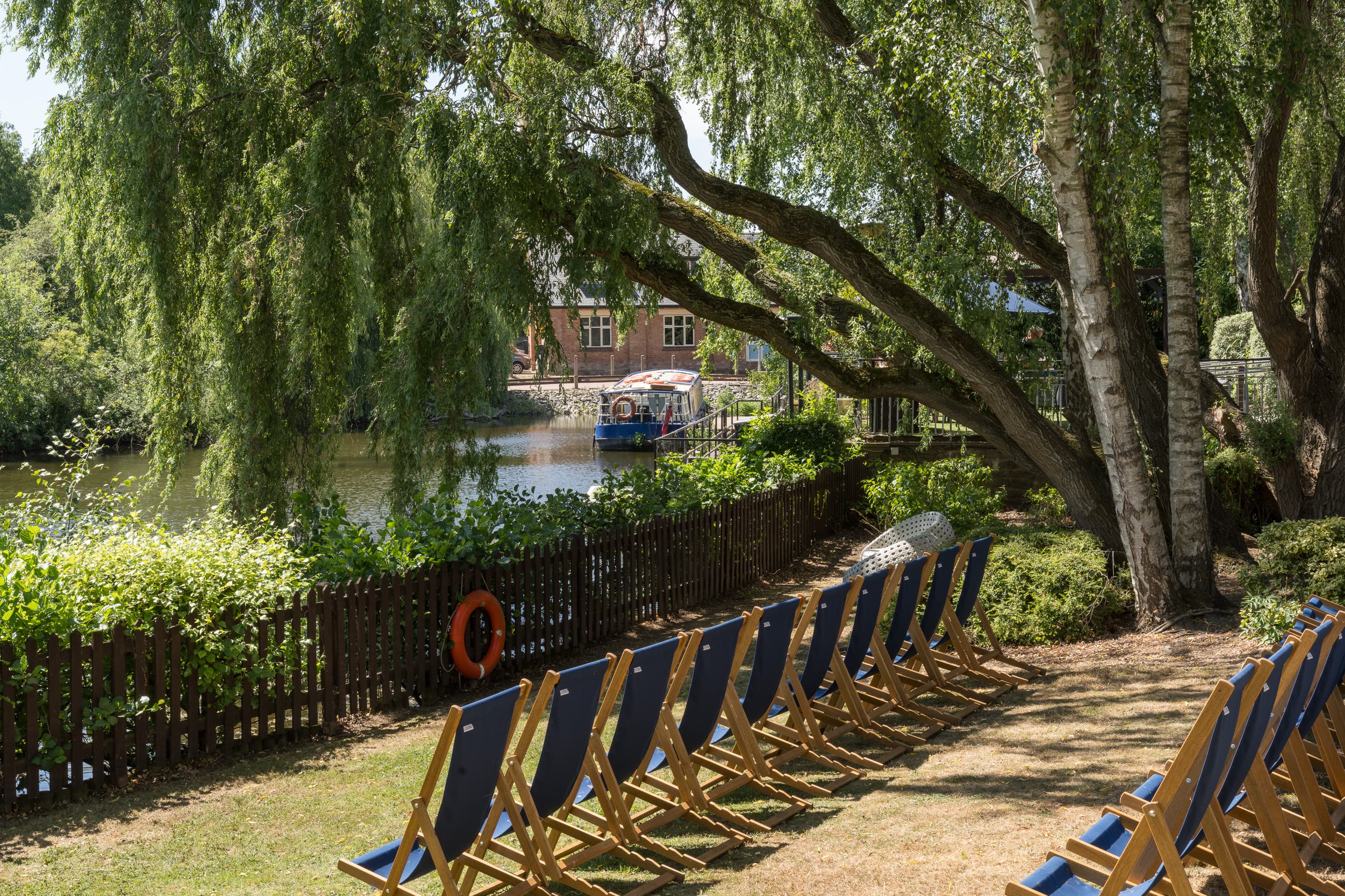 Rows of blue deckchairs on a sunny riverside lawn beside the River Avon.