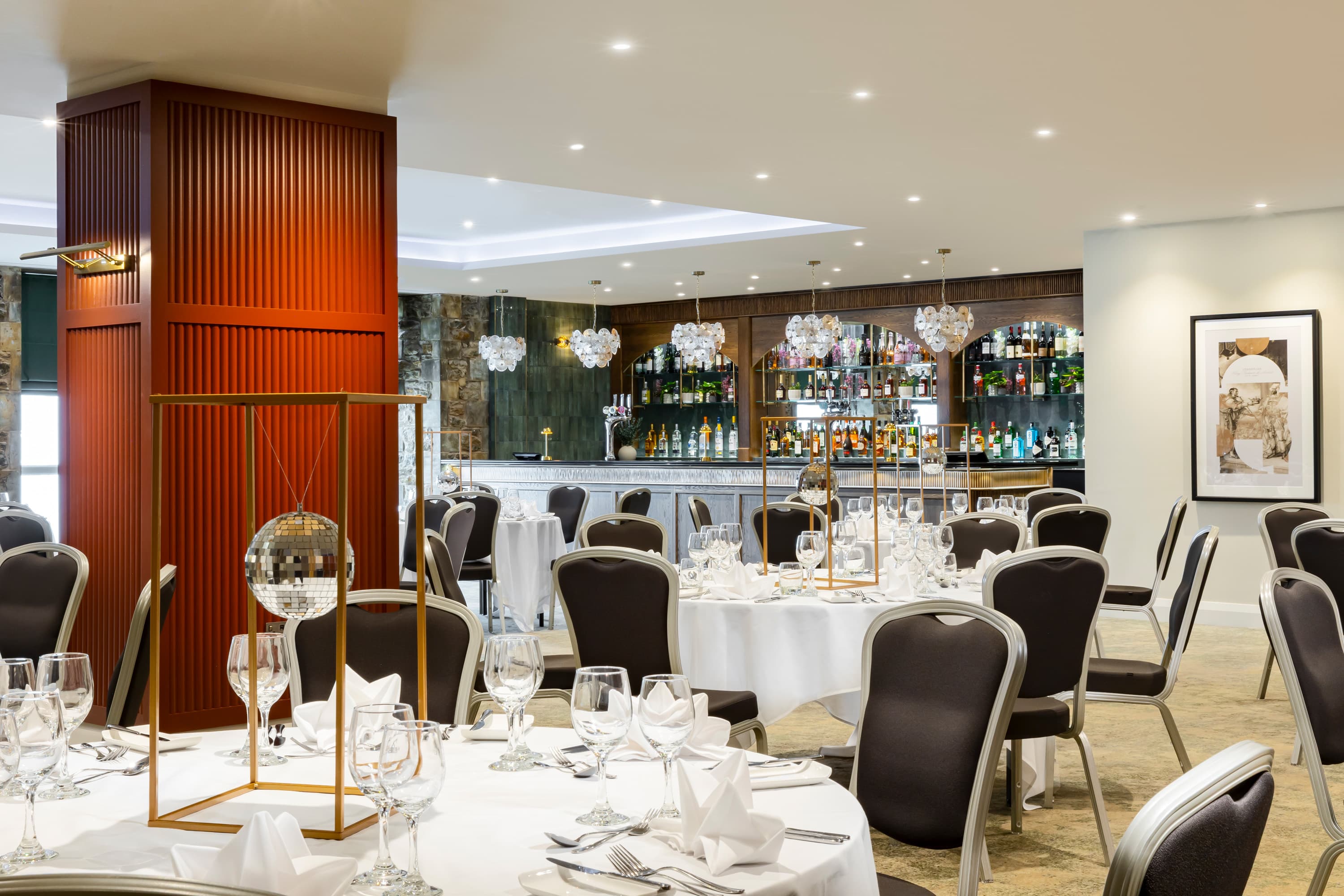 Banqueting room with round tables set for dining and a fully stocked bar beyond