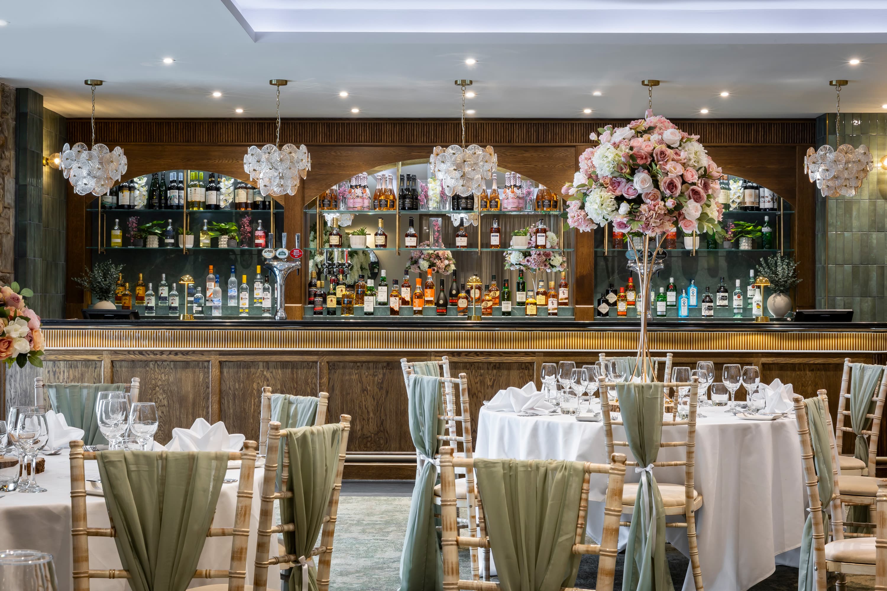 Elegantly dressed function room with a well-stocked bar and tall floral centrepieces.