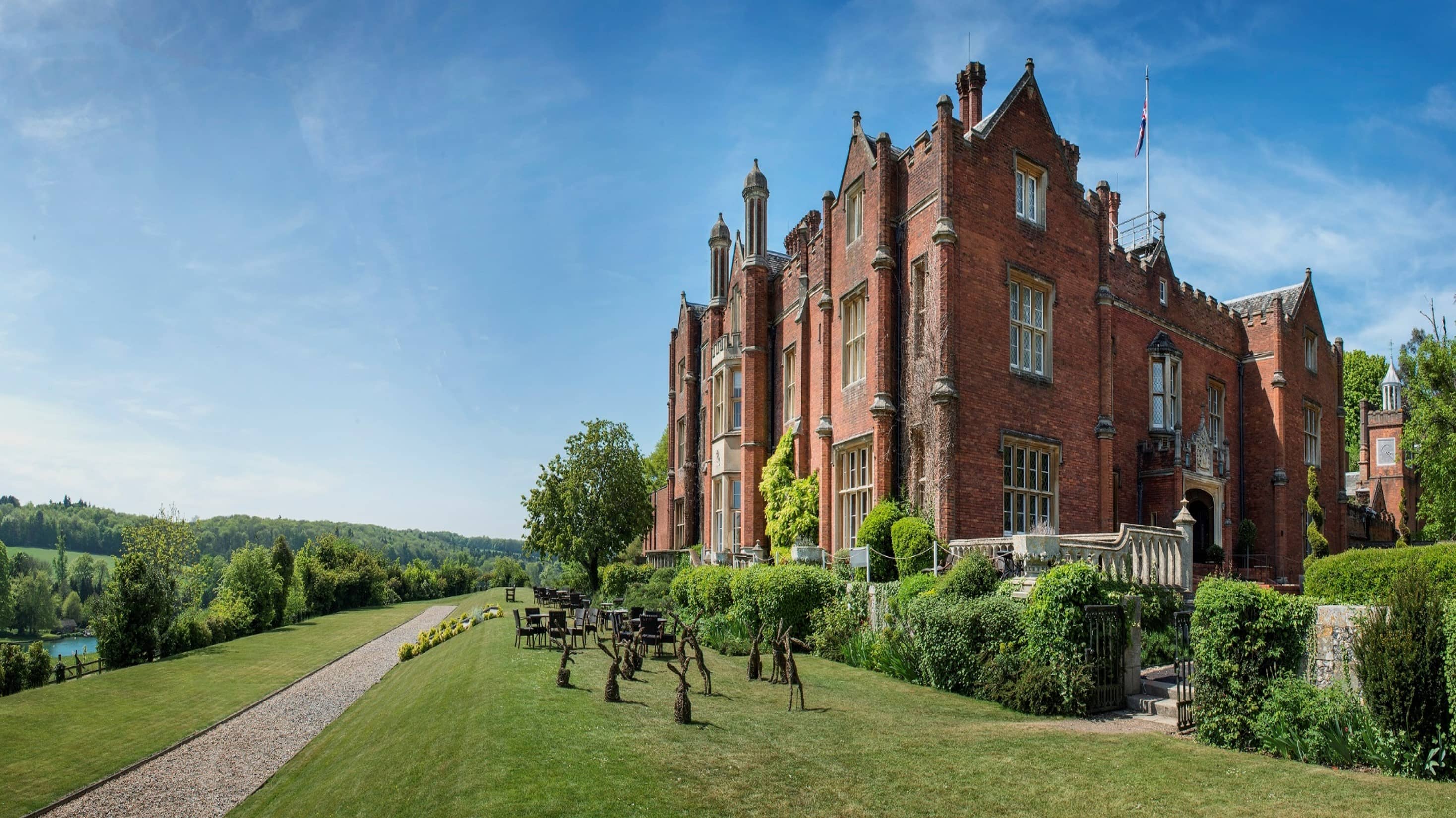 The red brick Victorian manor house exterior with manicured lawns and rolling countryside views.