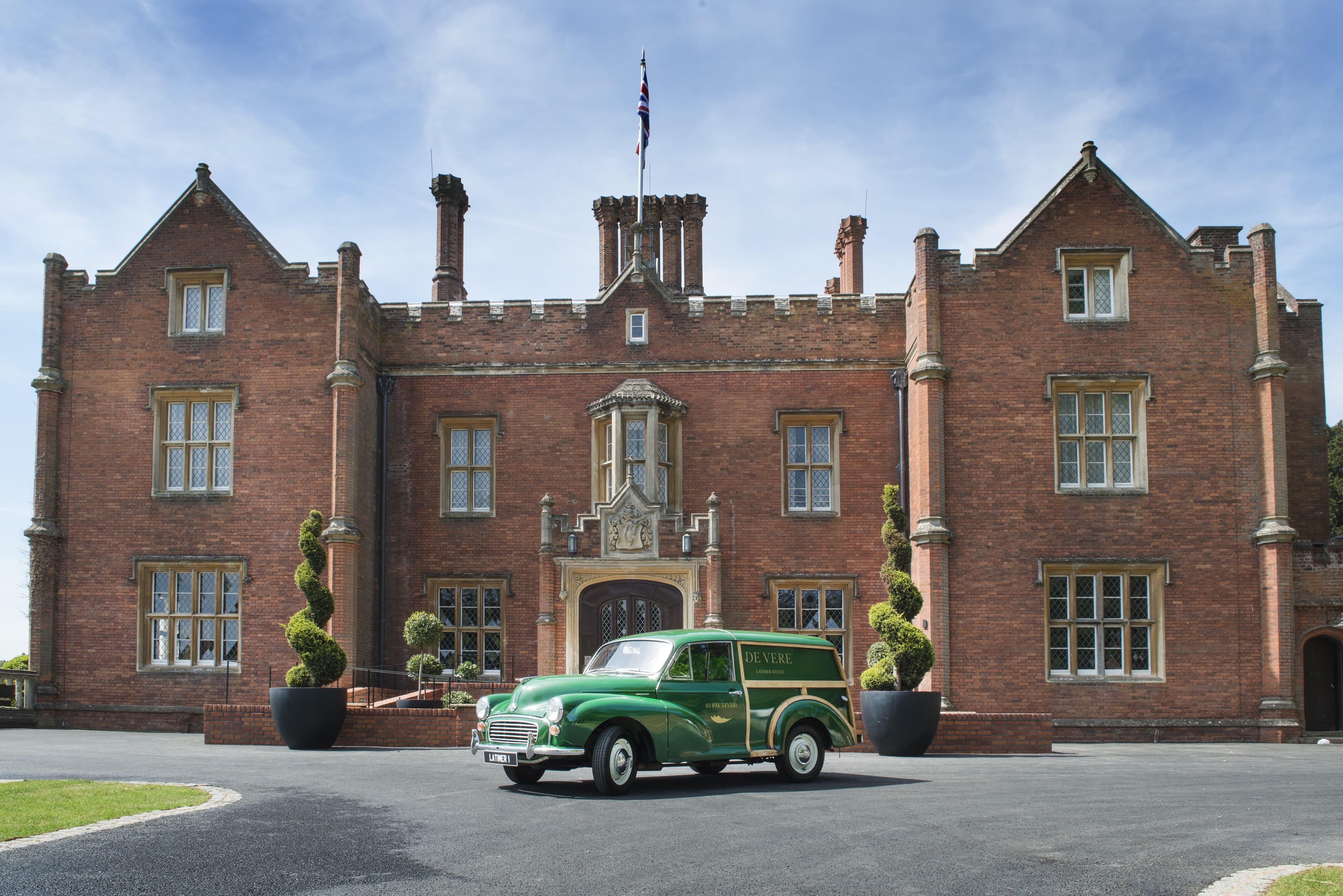 The red brick Tudor manor exterior with a vintage green De Vere van parked outside.