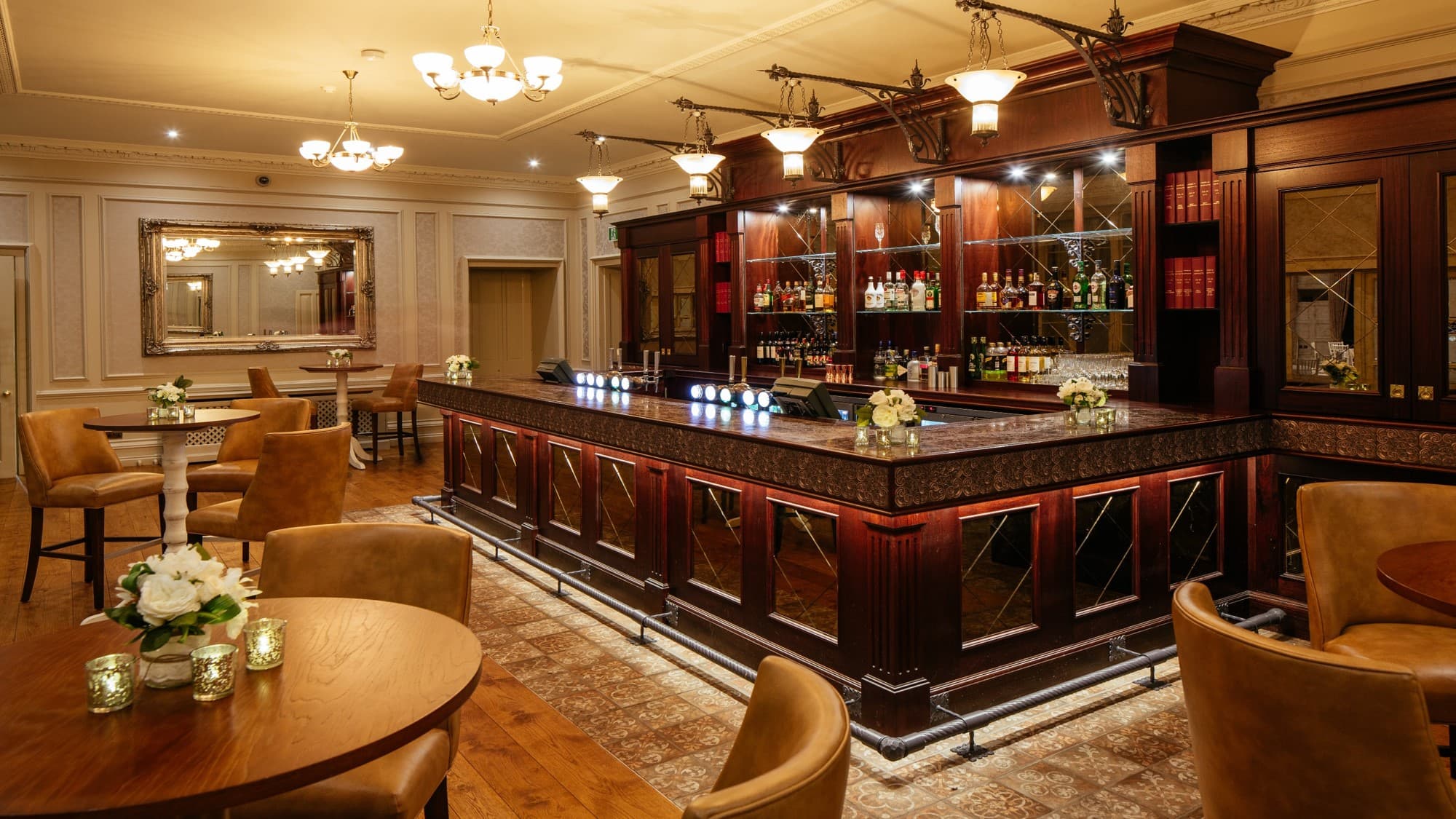 Elegant hotel bar with dark wood fittings, leather seating and chandelier lighting.