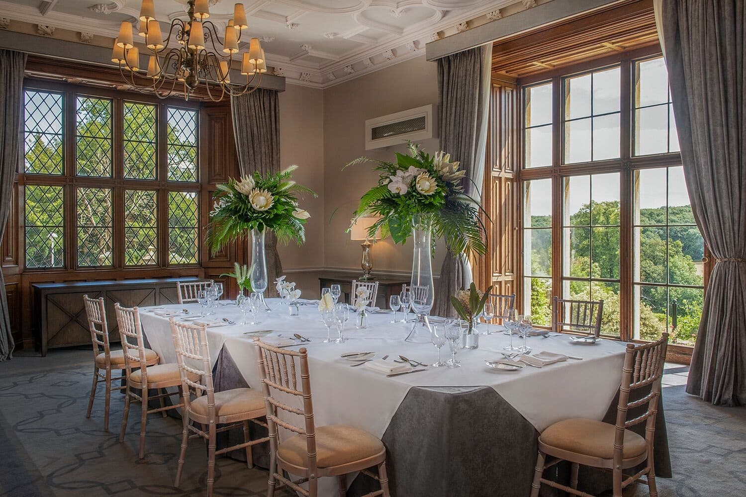 Private dining room with oval table, chiavari chairs and tall floral centrepieces at De Vere Latimer Estate.