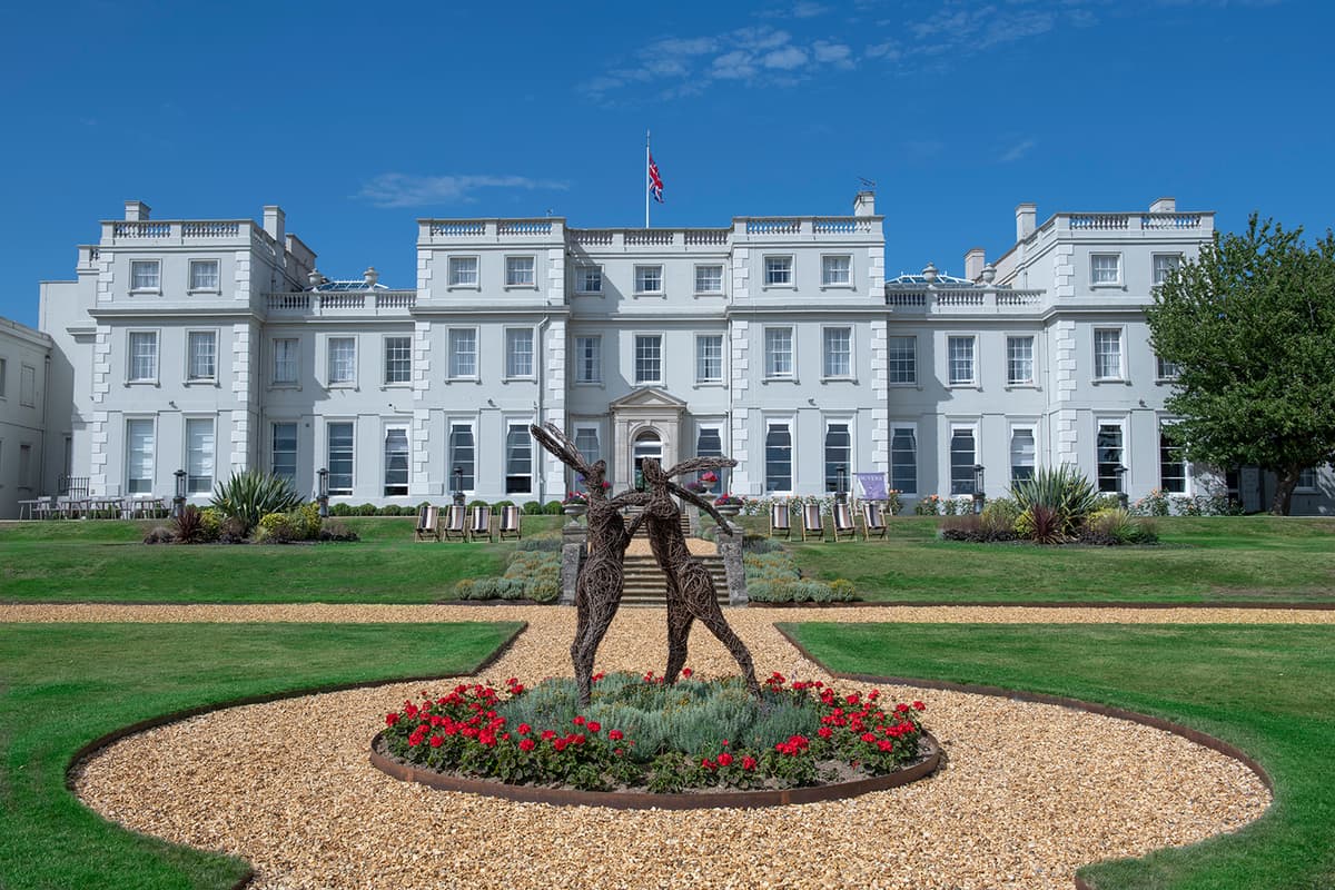The grand white Georgian exterior of De Vere Wokefield Estate with wire hare sculptures.