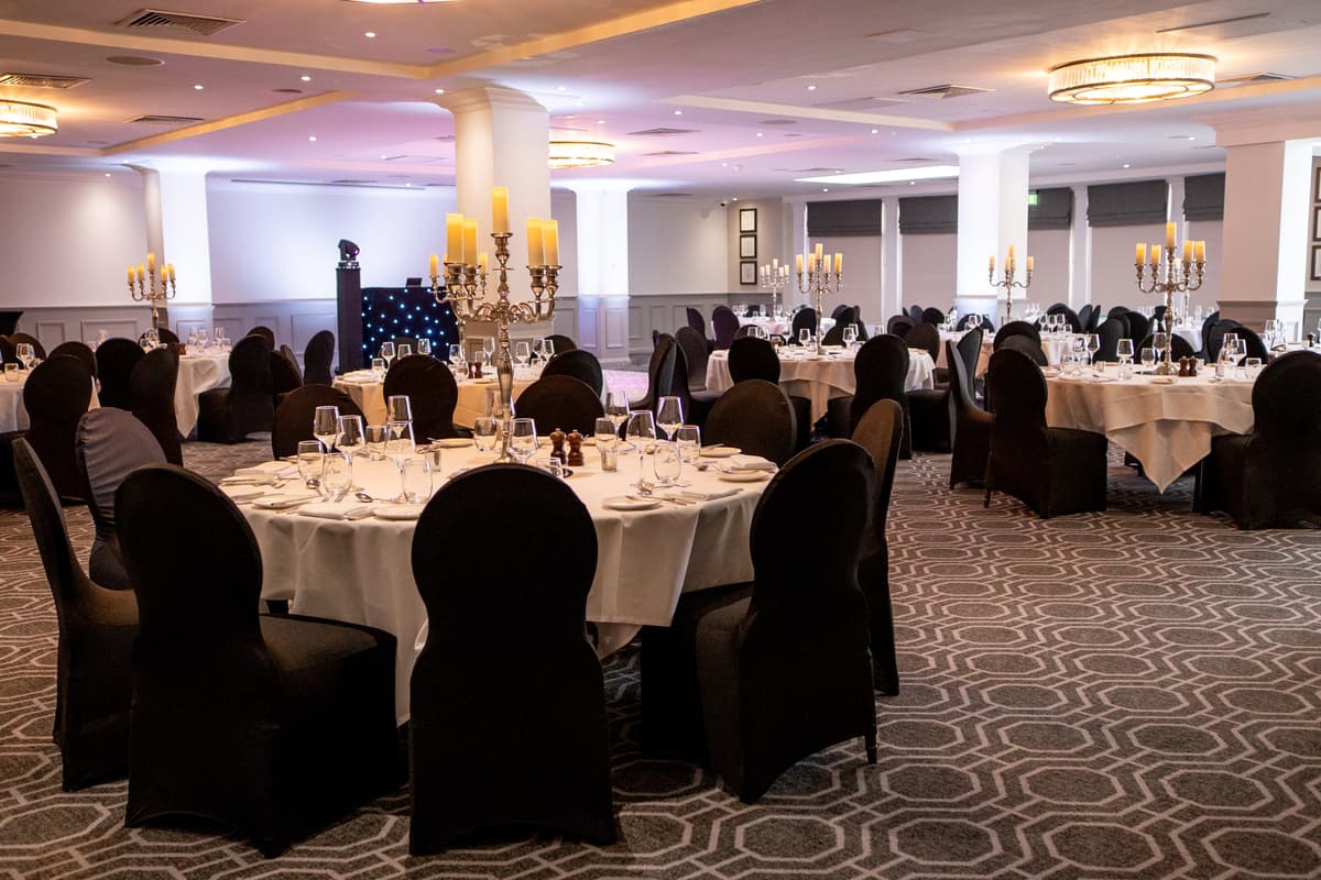 Ballroom at De Vere Wokefield Estate laid for a formal dinner with round tables, black chair covers and silver candelabras.