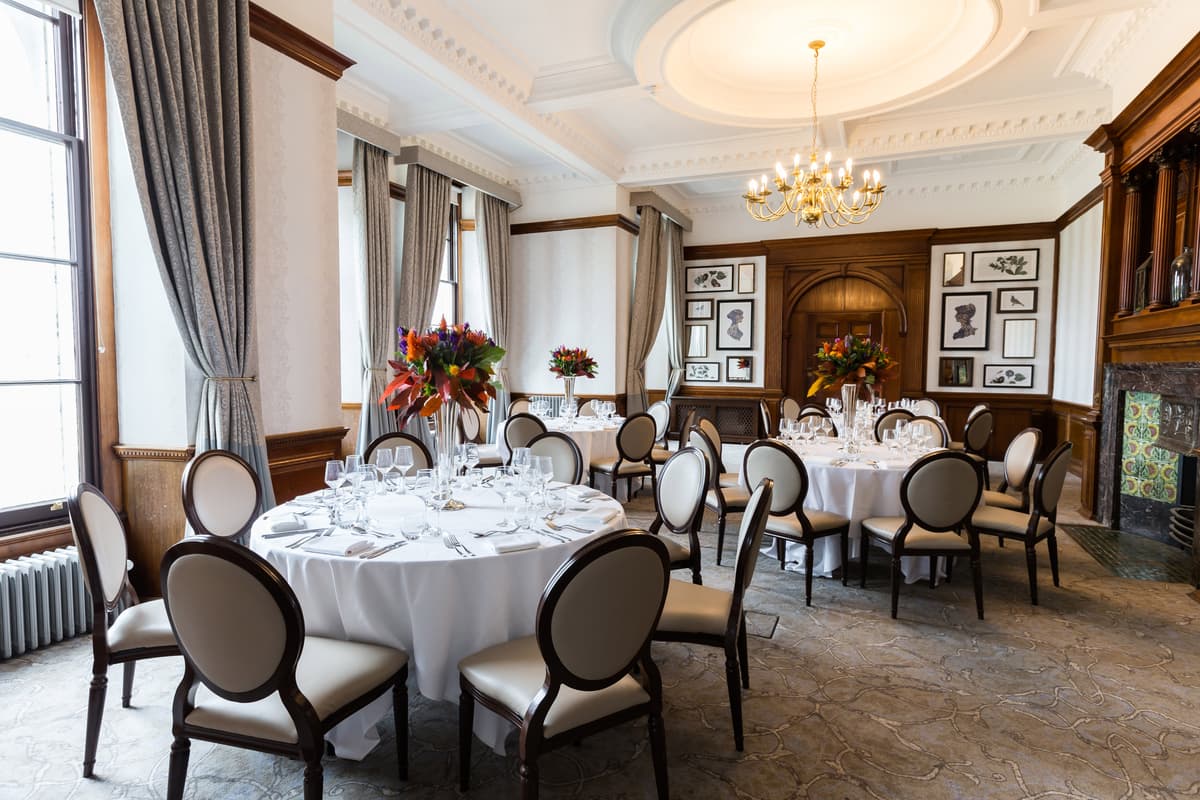 Elegant private dining room with round tables, chandelier and ornate plasterwork ceiling.