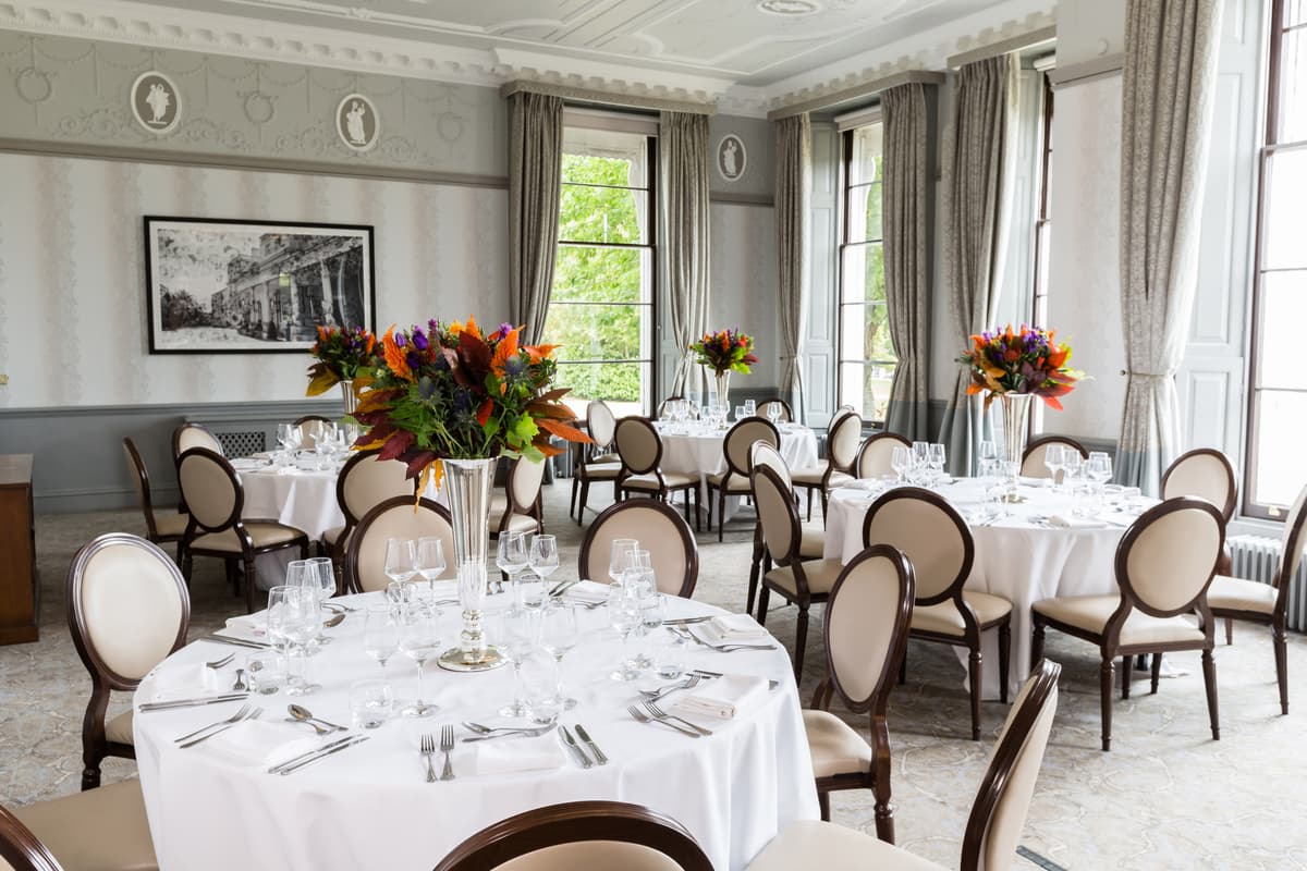 Elegant private dining room with round tables, floral centrepieces and ornate plasterwork ceiling.