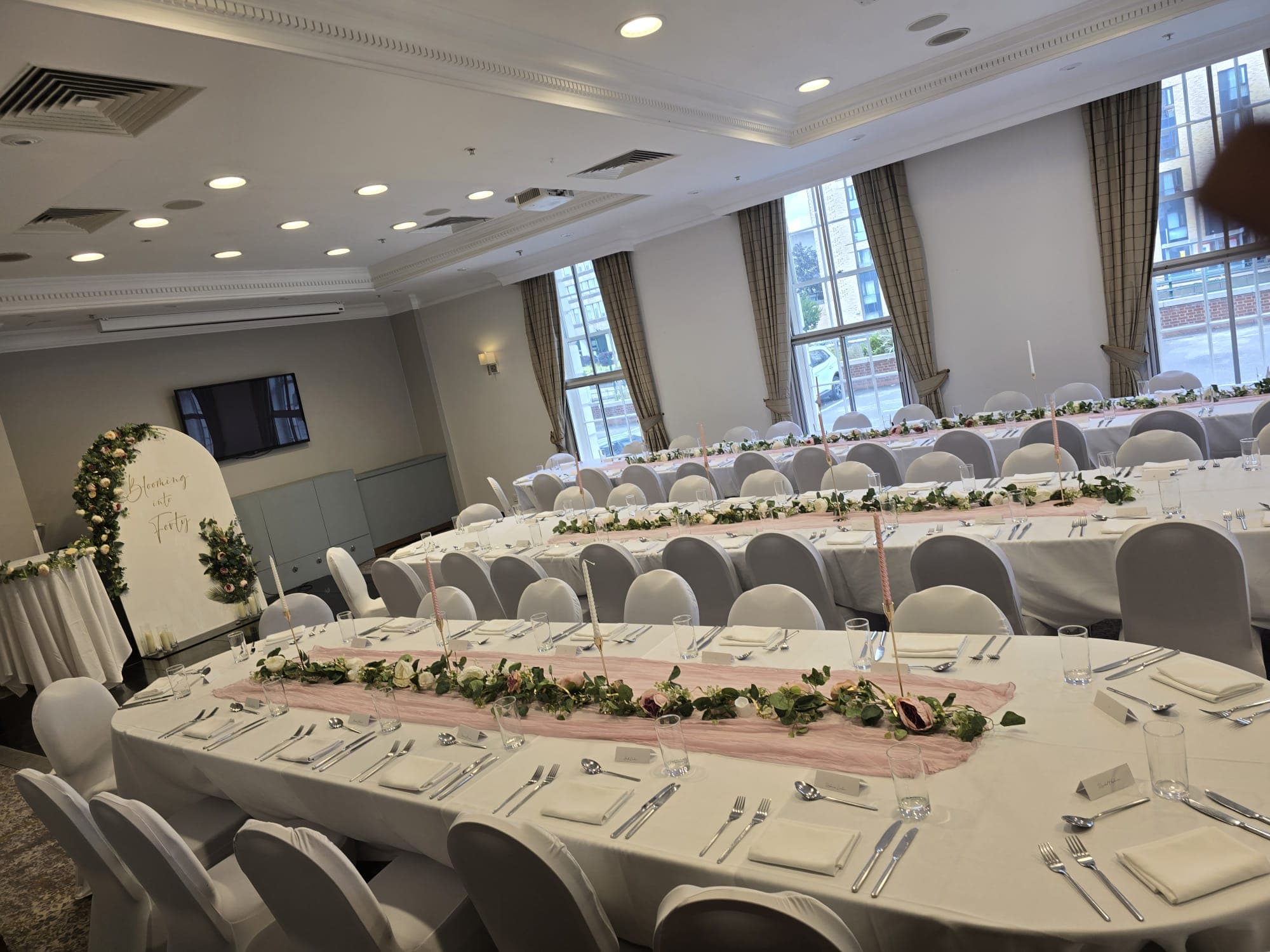 Banqueting room set for a celebration with floral table runners and grey chair covers.