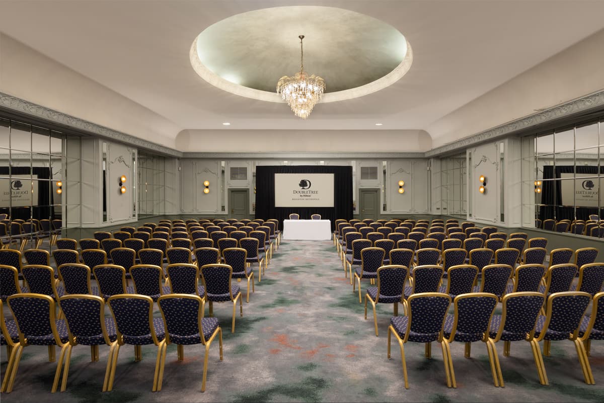 Theatre-style conference room with gold and navy chairs, chandelier and projection screen.