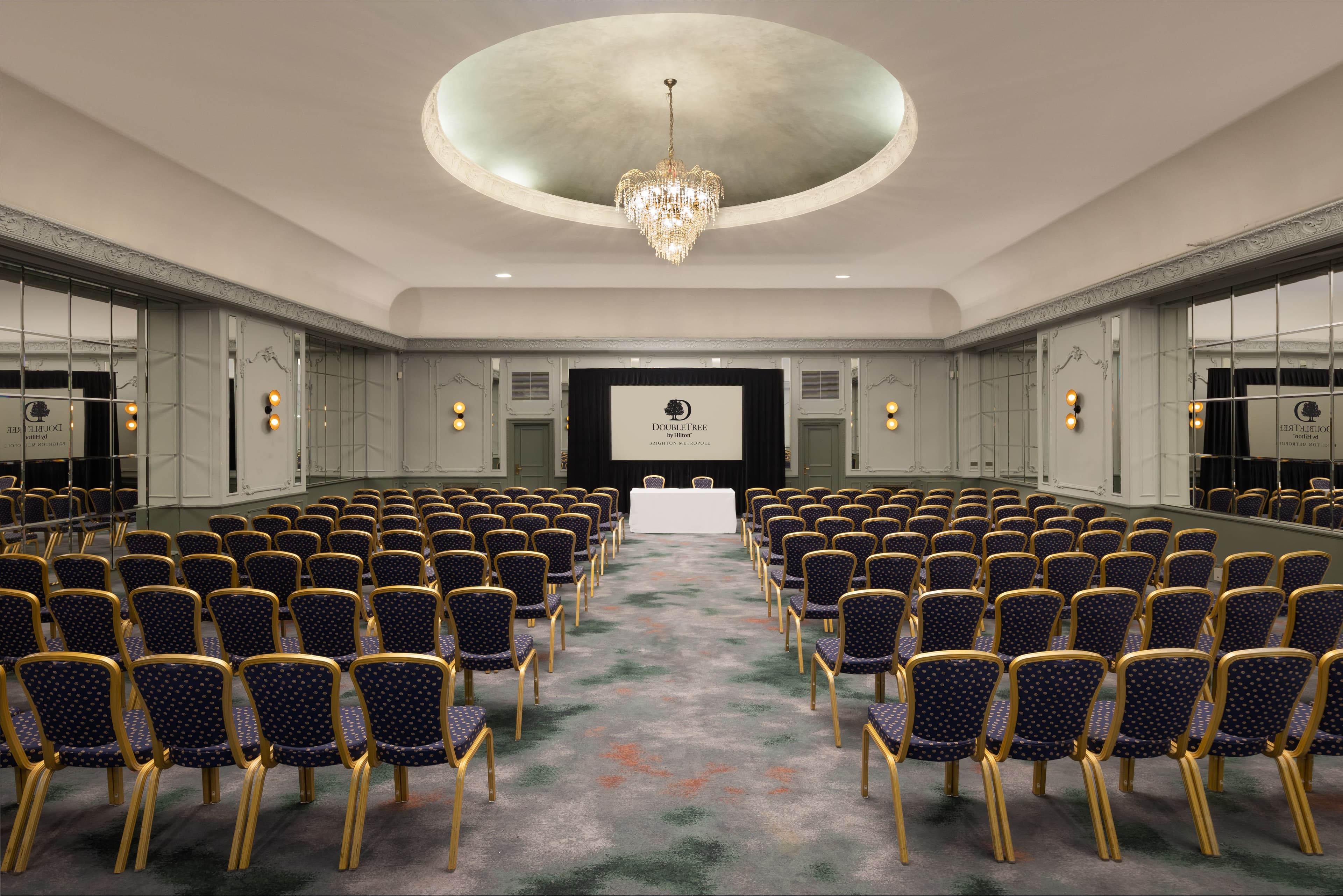 Theatre-style conference room with gold and navy chairs, chandelier and projection screen.