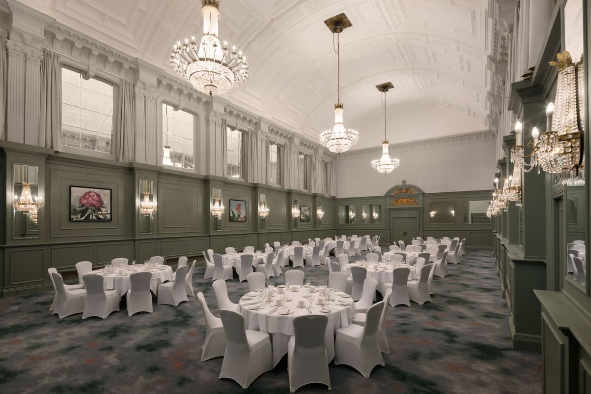 Grand ballroom with crystal chandeliers, round tables and white chair covers laid for dining.