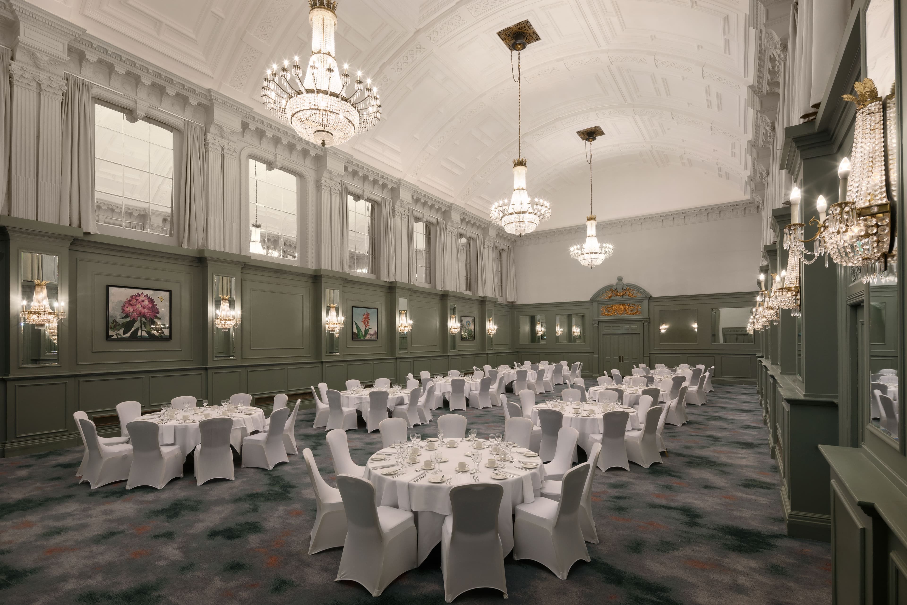 Grand ballroom with crystal chandeliers, round tables and white chair covers laid for dining.