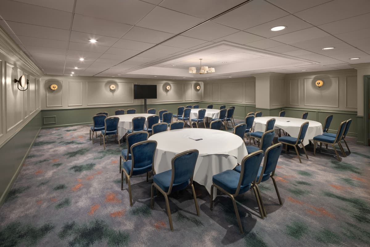 Private function room with round tables, blue banquet chairs and wall-mounted screen.