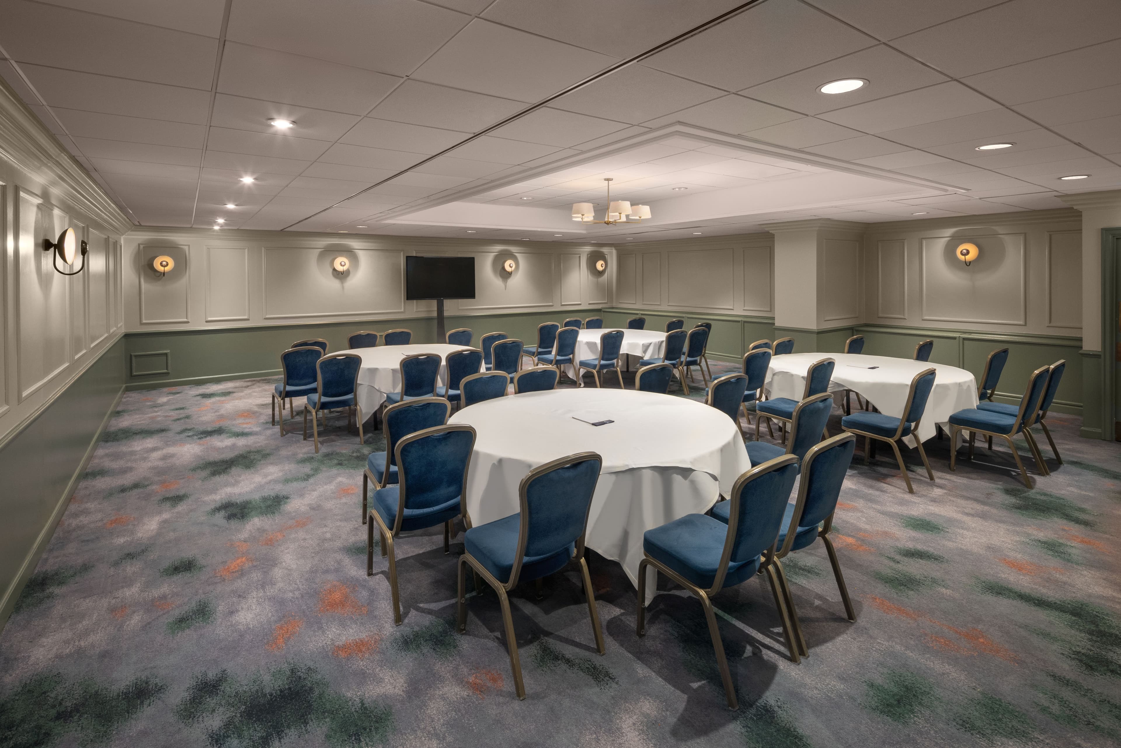 Private function room with round tables, blue banquet chairs and wall-mounted screen.