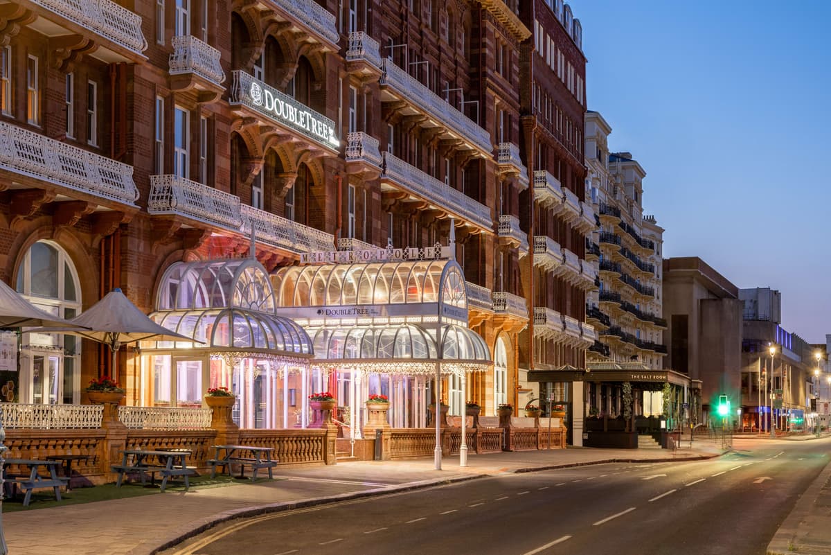 The illuminated Victorian red-brick exterior of the DoubleTree Brighton Metropole at dusk.