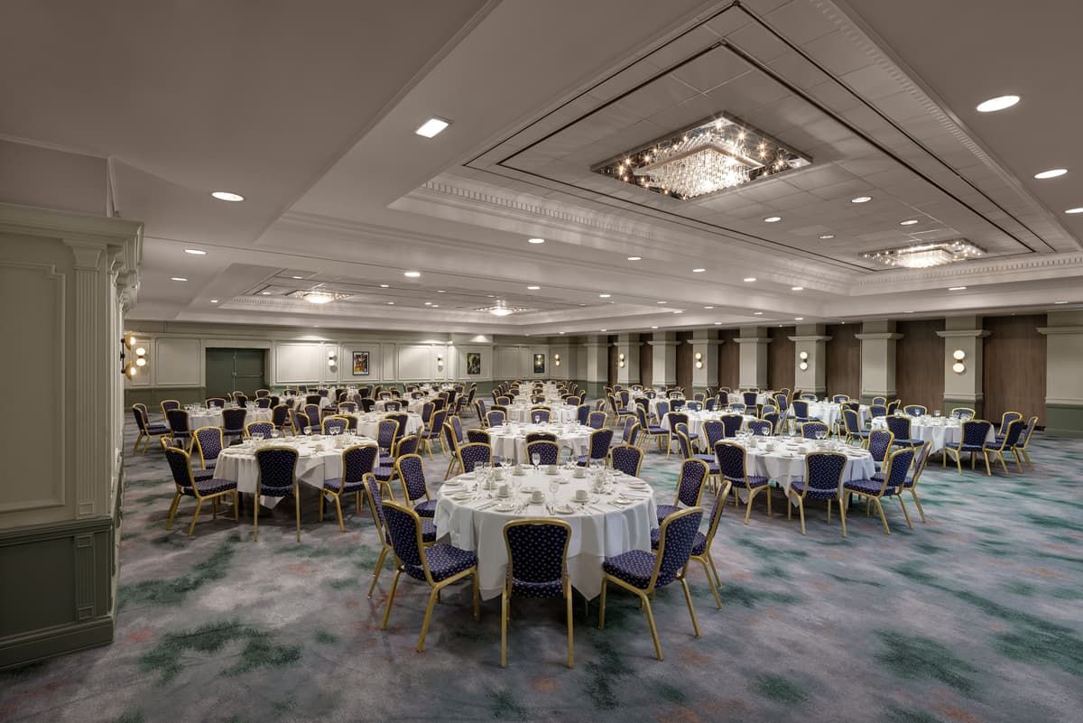 Large ballroom laid for a banquet with round tables, blue chairs and a crystal chandelier.