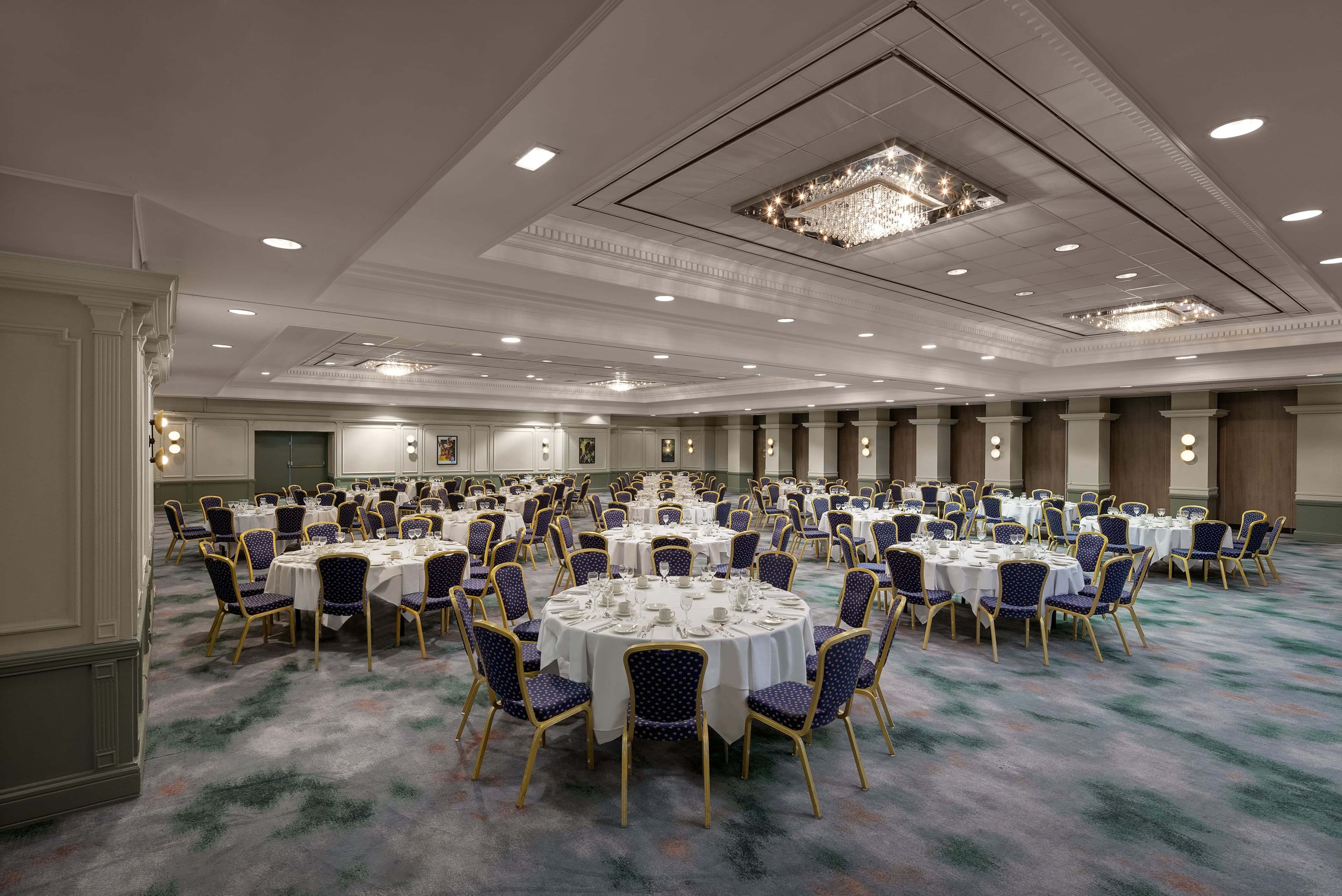 Large ballroom laid for a banquet with round tables, blue chairs and a crystal chandelier.