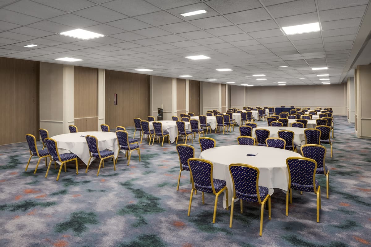 Large hotel function room with round tables, white linen and blue banqueting chairs.