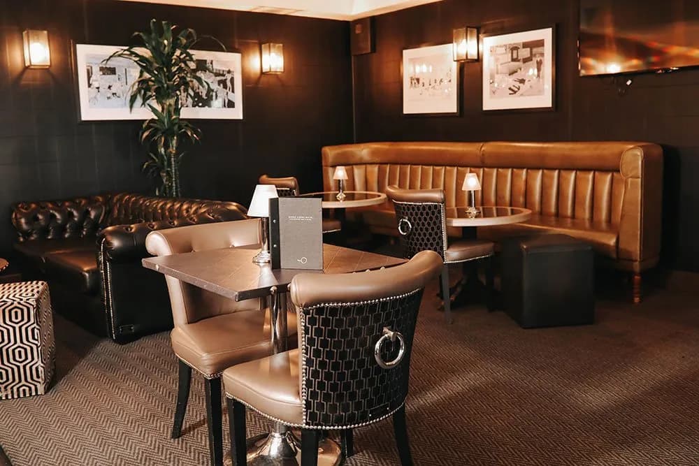 Dimly lit hotel bar lounge with tan leather banquette seating and framed artwork.