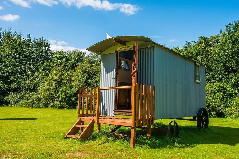 Shepherd's hut with wooden steps and veranda set in a sunny green garden.
