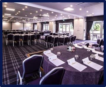 Spacious conference room with round tables, blue chairs and large windows at DoubleTree Cheltenham.