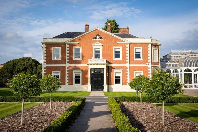 Red brick Georgian manor house exterior with formal gardens and a glass conservatory.