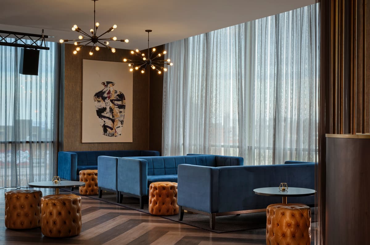 Stylish rooftop bar with blue velvet sofas, tan ottomans and a sputnik chandelier.
