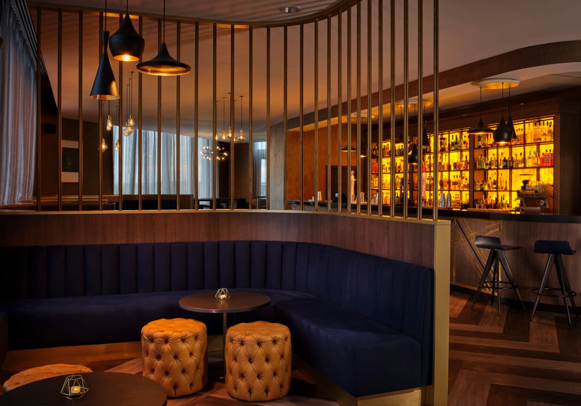 Curved navy banquette seating beside a warmly lit backlit spirits bar at DoubleTree Hull.
