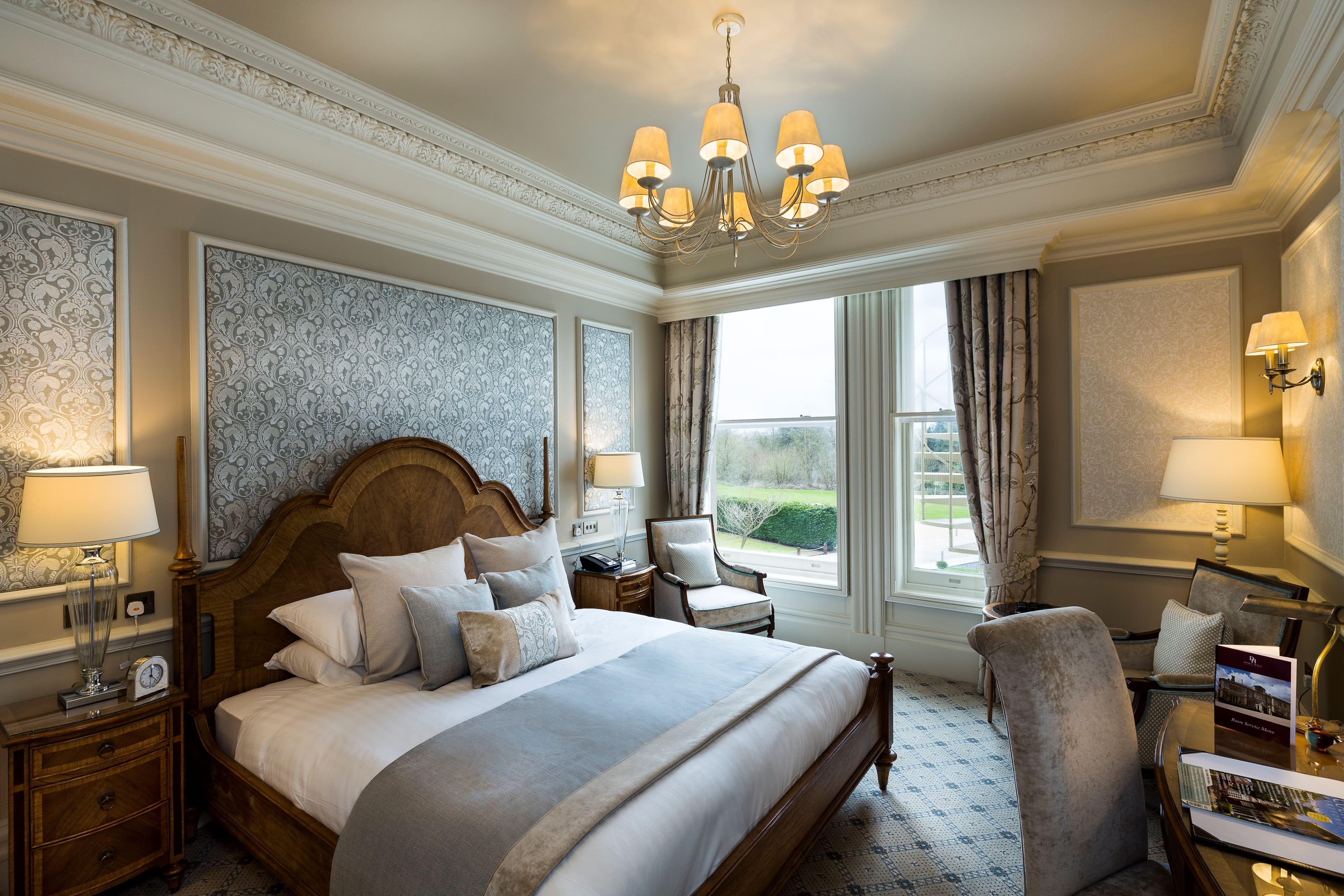Elegantly furnished double bedroom with ornate cornicing, chandelier and garden views.