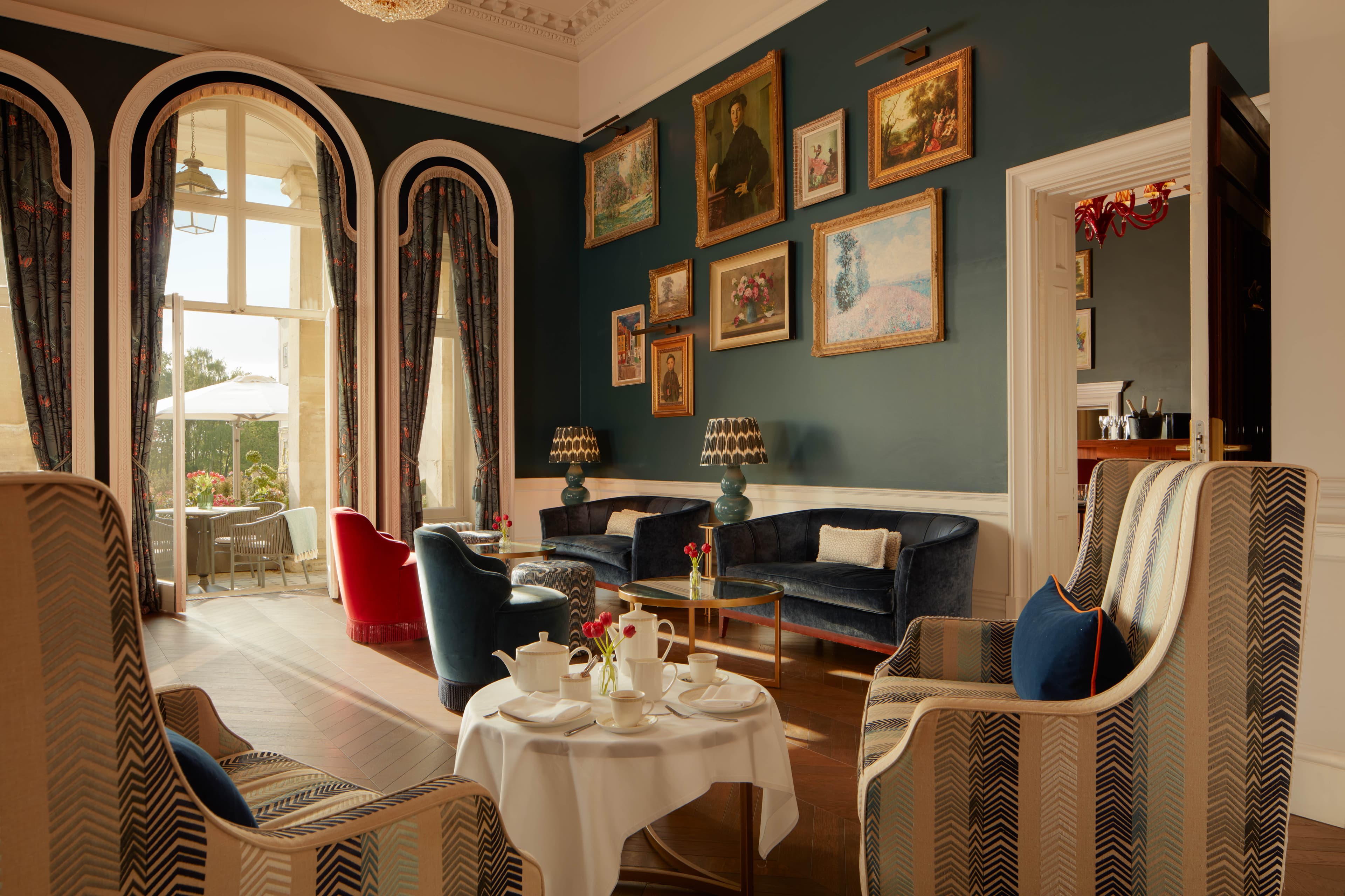 Teal drawing room with gilt-framed paintings, velvet sofas, striped armchairs and afternoon tea on a white table