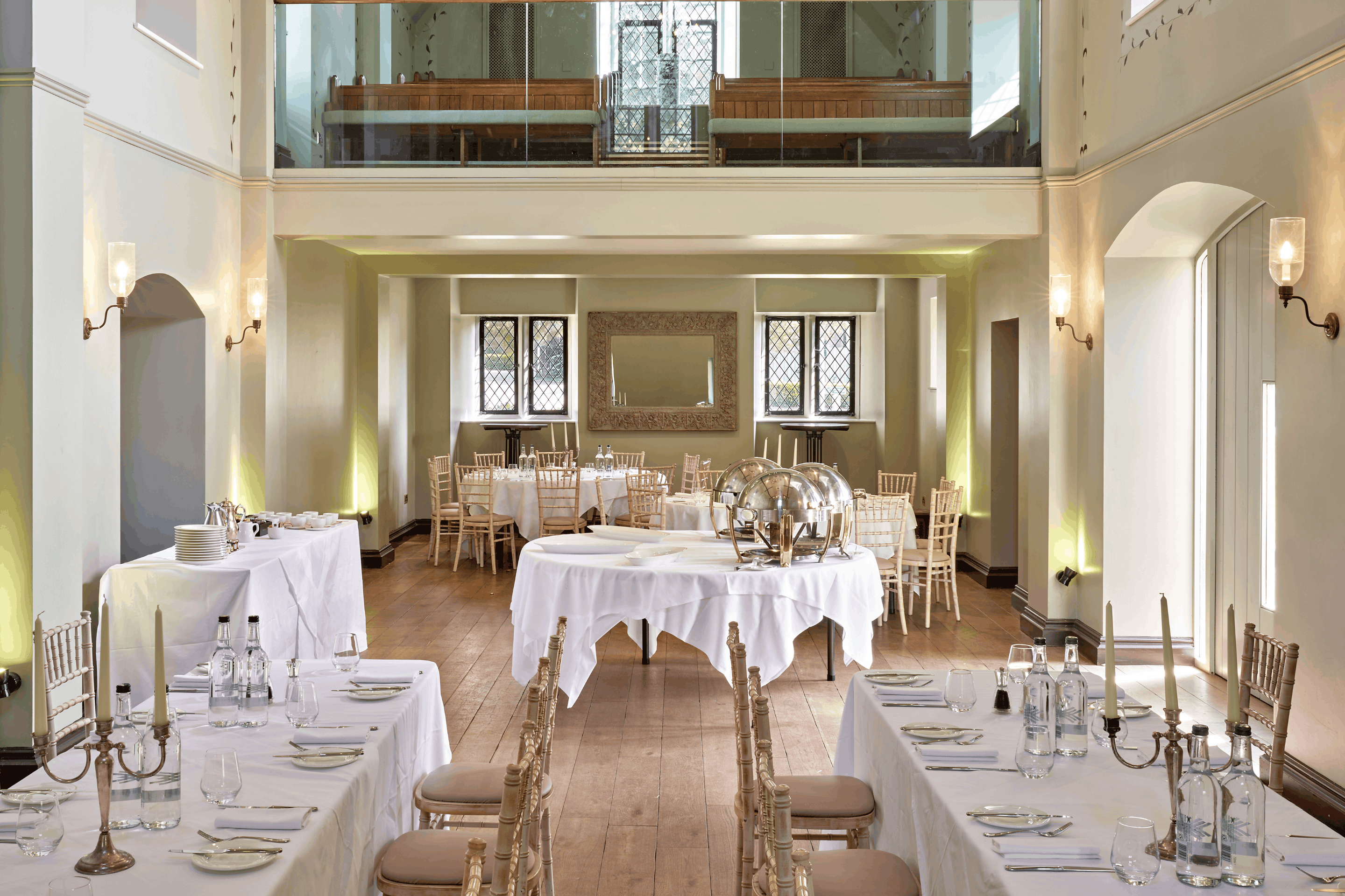 Bright private dining room with white linen tables, chiavari chairs and a mezzanine gallery above.