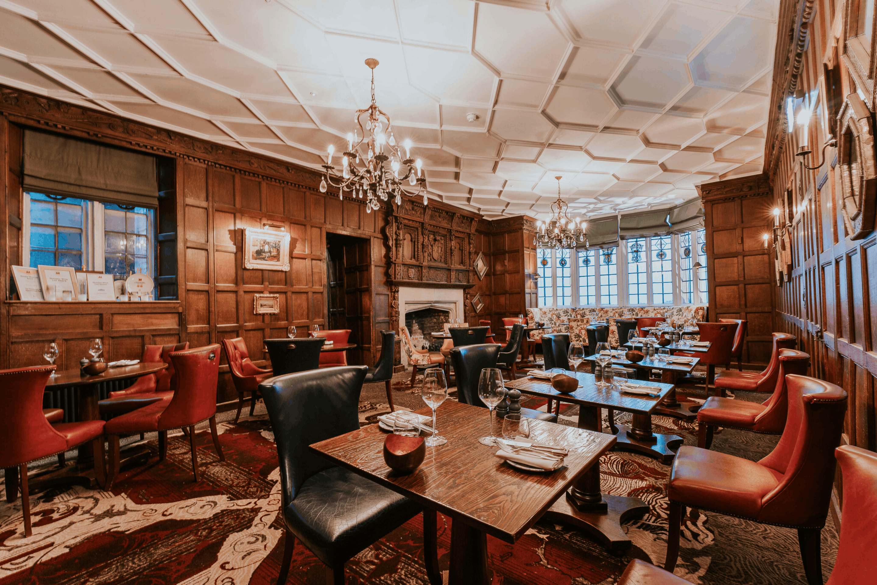 Panelled dining room with crystal chandeliers, leather chairs and an ornate stone fireplace.