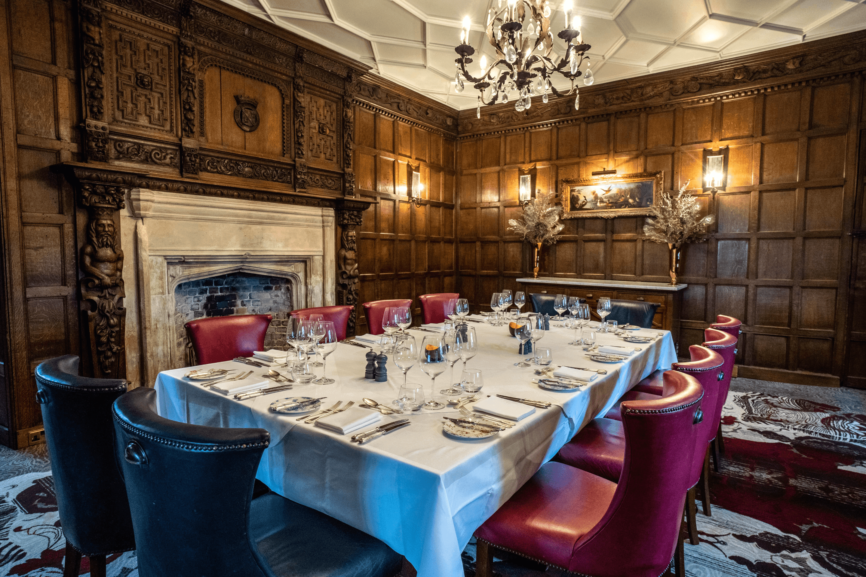 Panelled private dining room with a stone fireplace, chandelier and laid table at Ellenborough Park.