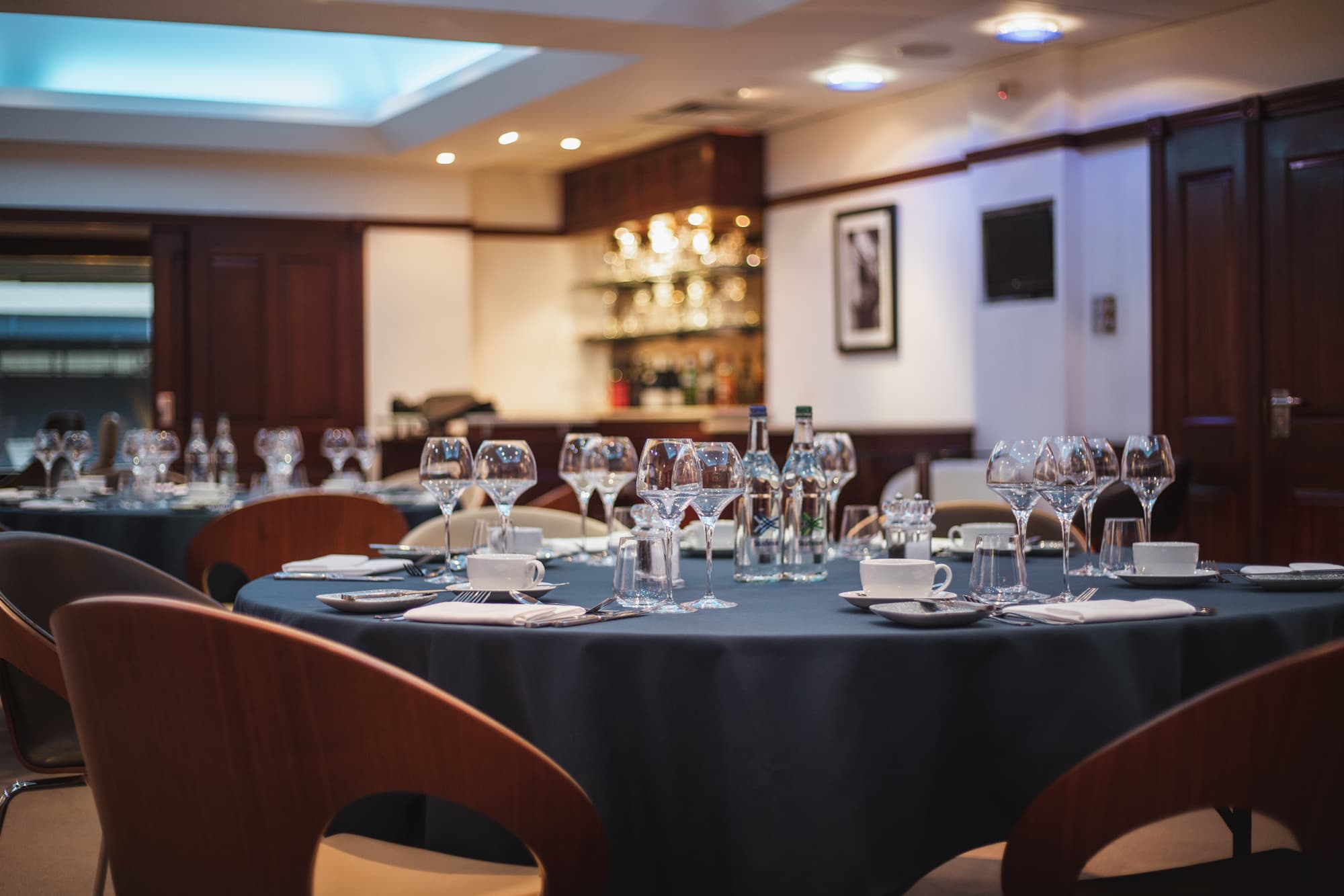 Formally laid round tables with wine glasses and blue linen in a private dining room.