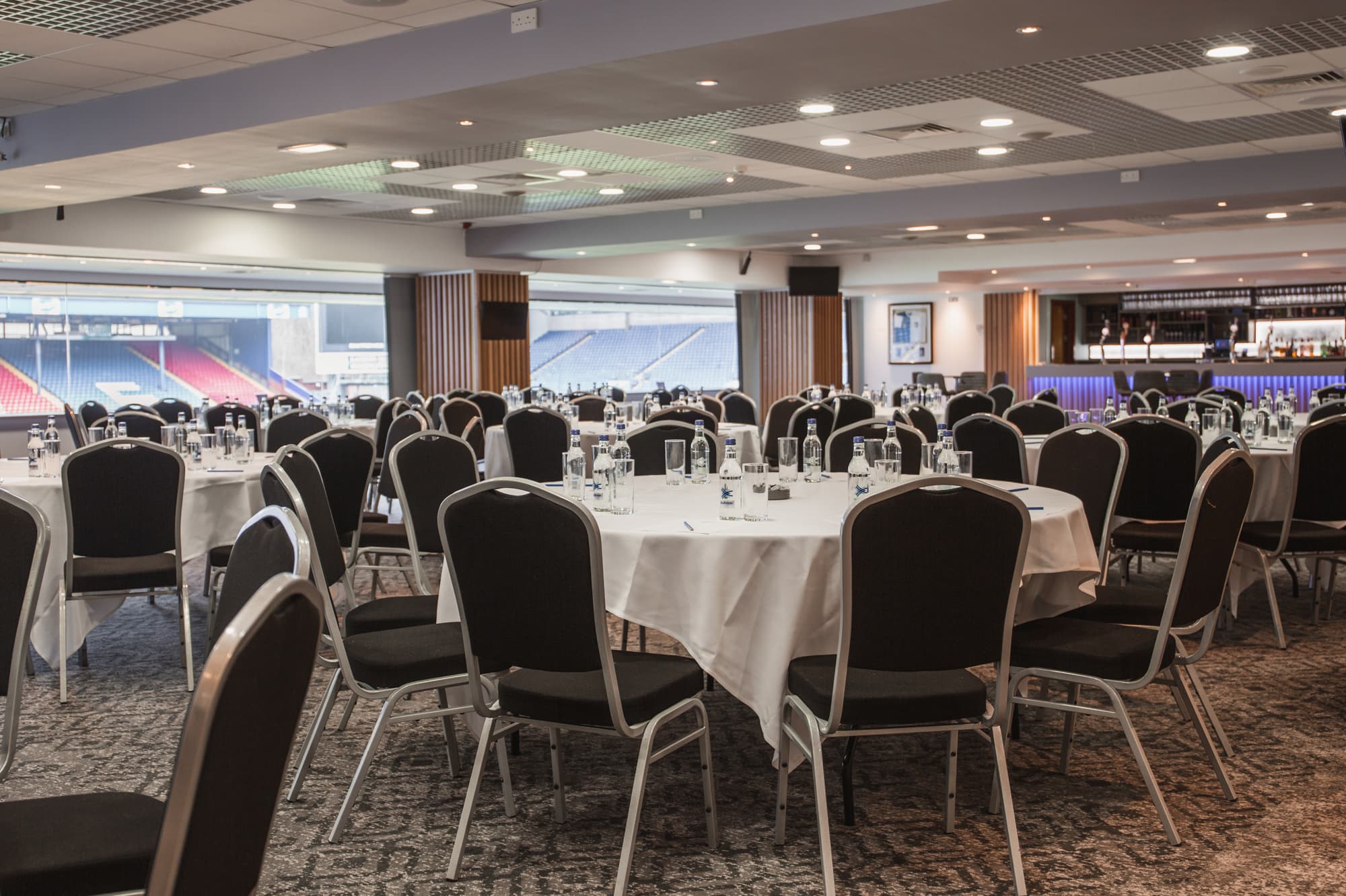 Banqueting suite set for an event with round tables and stadium views beyond.