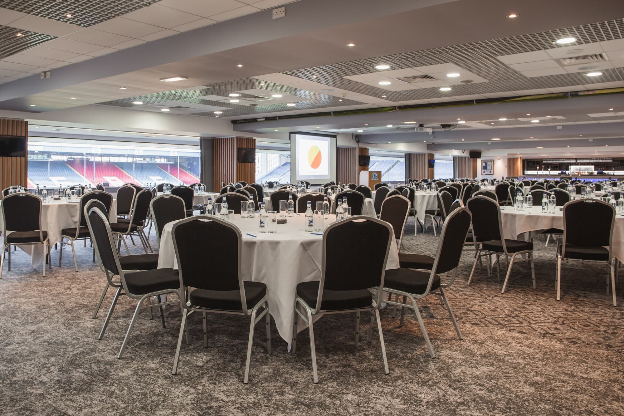 Large function room with round tables set for a conference overlooking the football stadium stands.