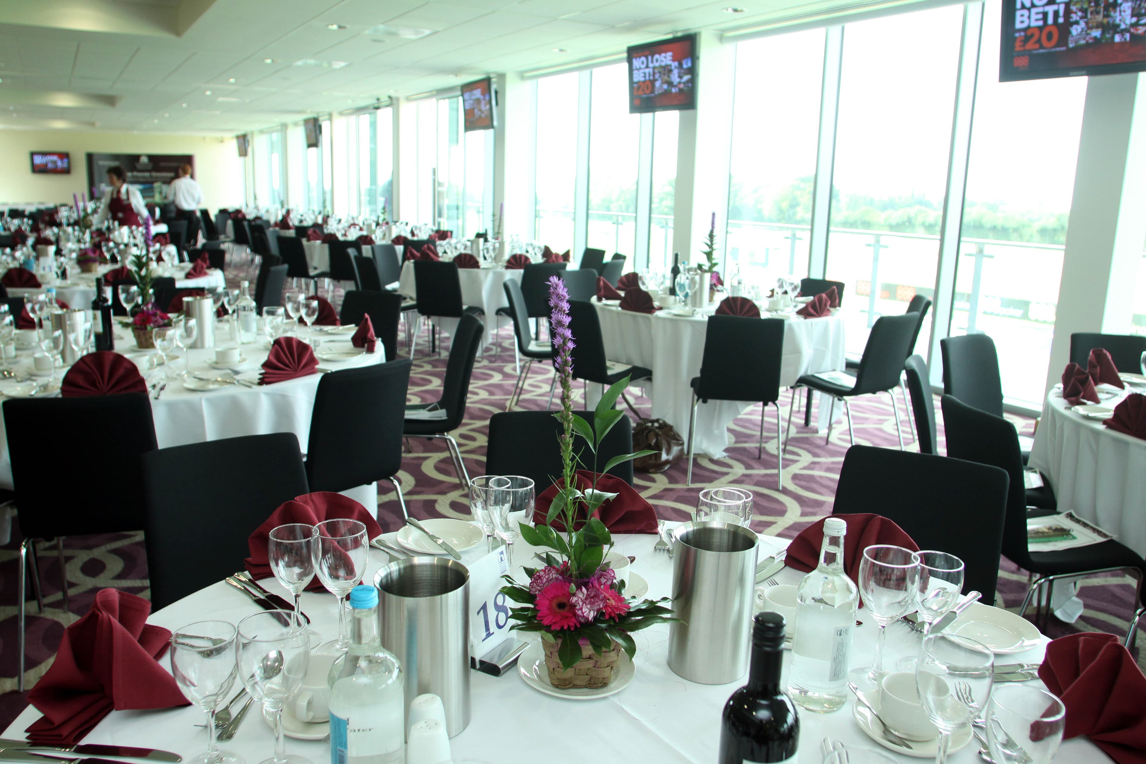 Racecourse function room laid for dining with floor-to-ceiling windows overlooking the track.
