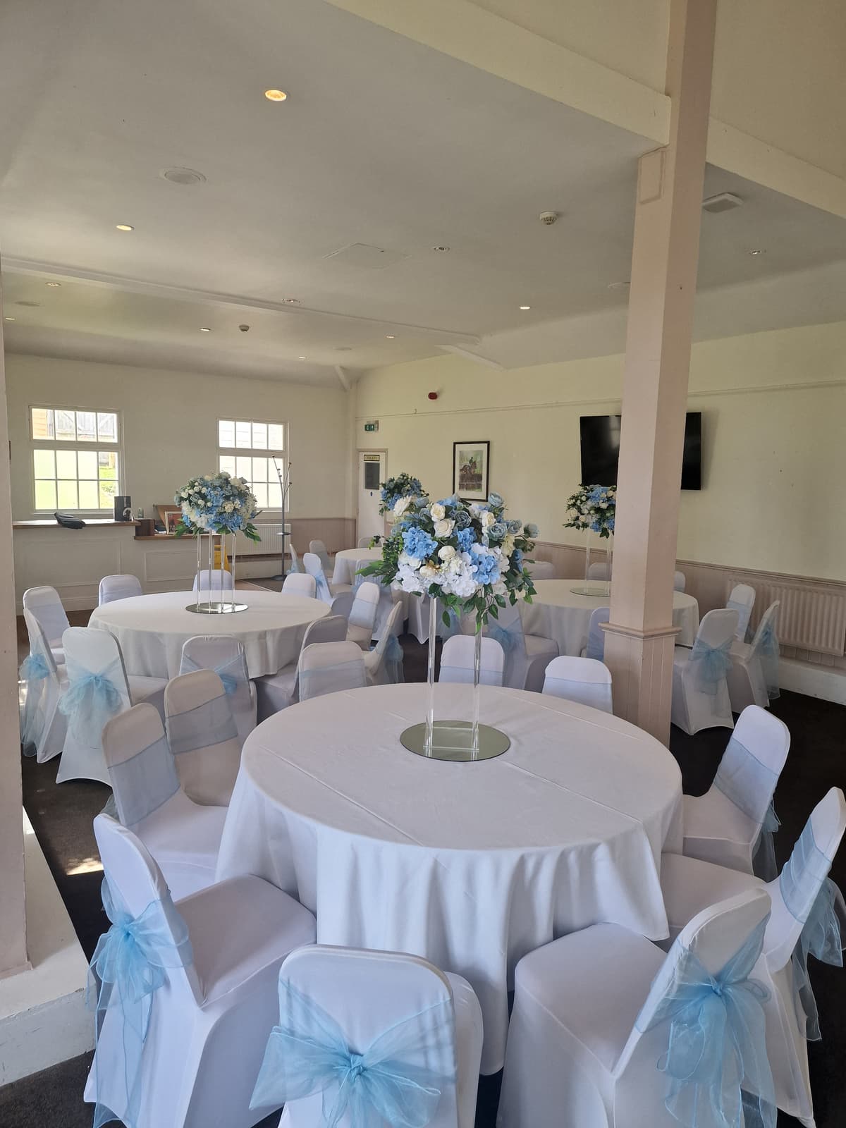 Function room at Fontwell Park Racecourse set with round tables and blue floral centrepieces.