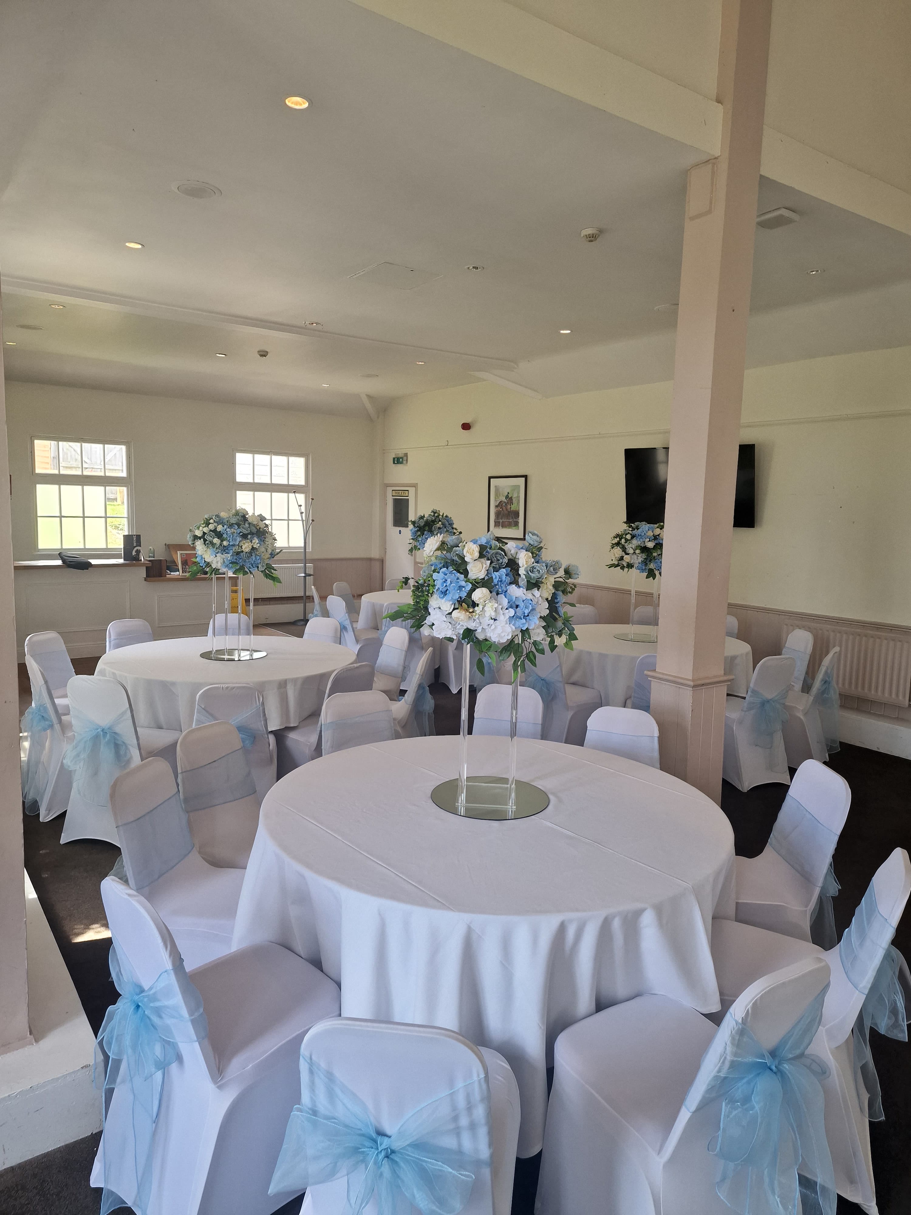 Function room at Fontwell Park Racecourse set with round tables and blue floral centrepieces.