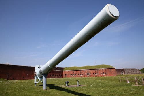 Large historic cannon displayed outdoors at Fort Nelson with red brick fortifications behind.