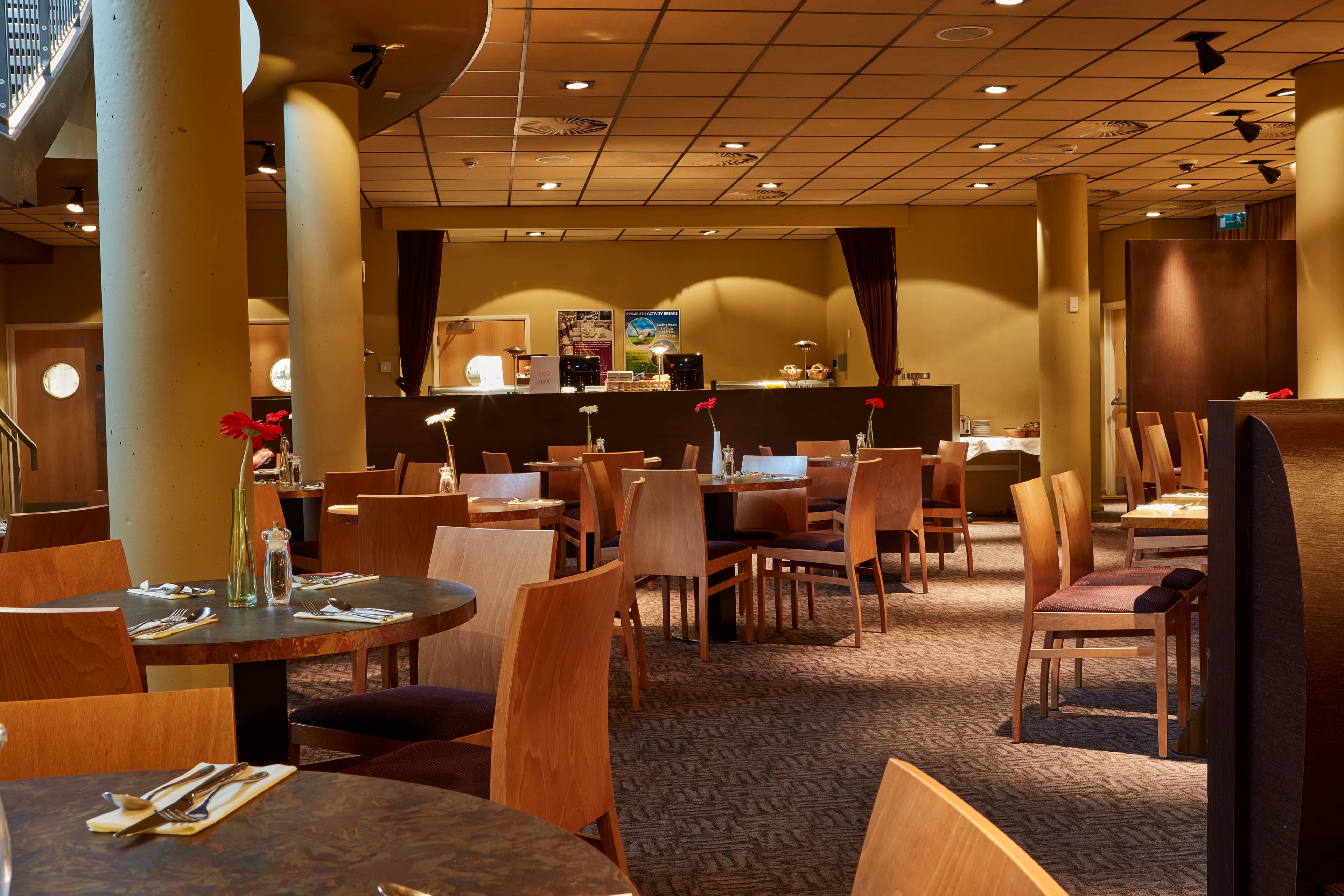 Hotel restaurant dining area with wooden chairs, round tables and laid cutlery settings.