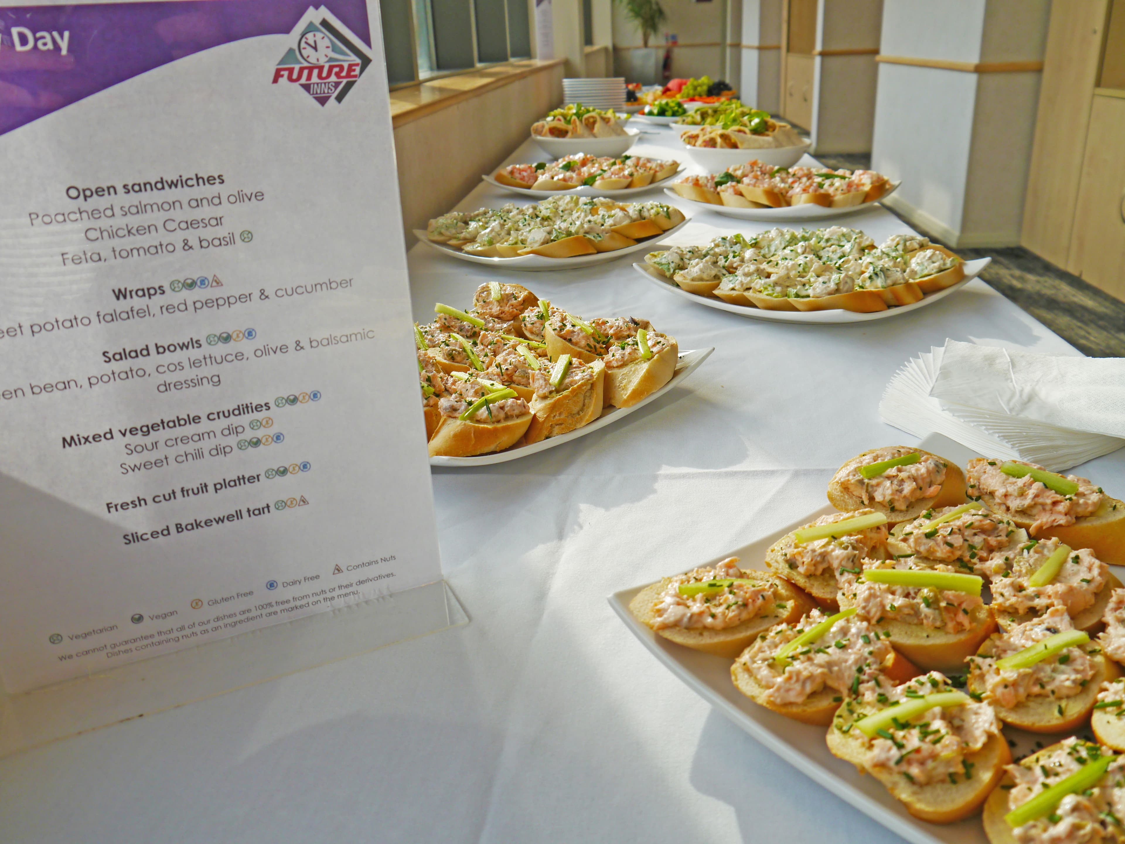 Platters of open sandwiches on a white-clothed buffet table with a Future Inns menu card.