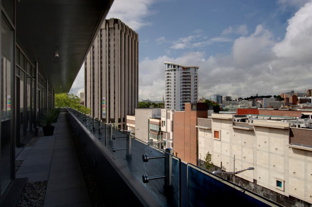 Narrow hotel terrace with glass balustrade overlooking Bristol city centre rooftops and towers.