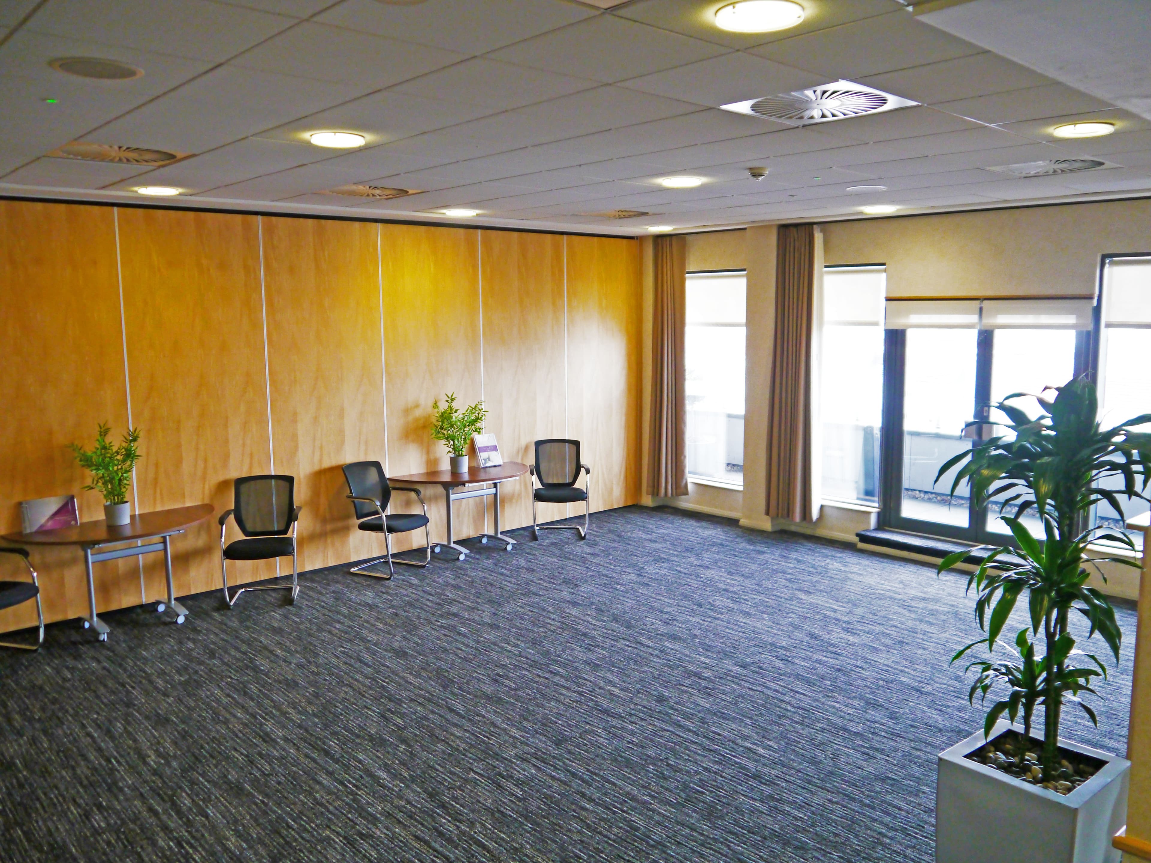 Spacious meeting room with wood-panelled dividers, mesh chairs, small tables and large windows.