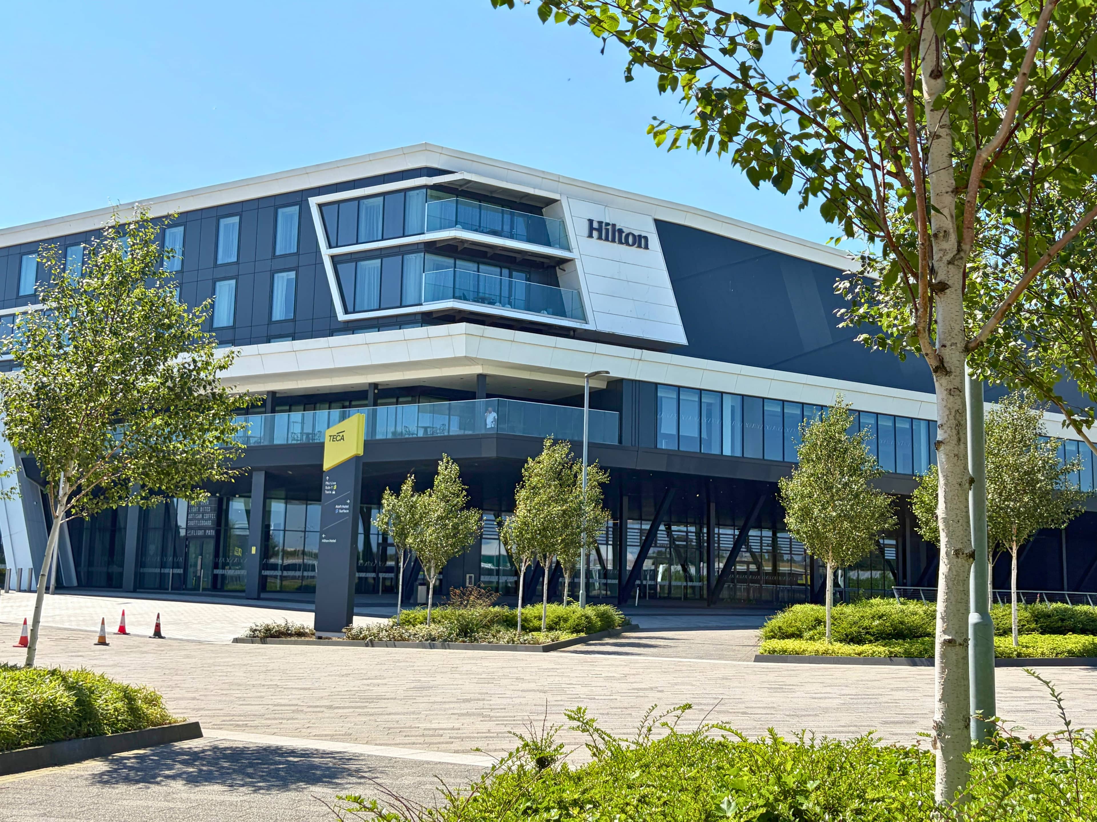 Exterior of the Hilton Aberdeen TECA hotel on a clear sunny day with landscaped grounds.