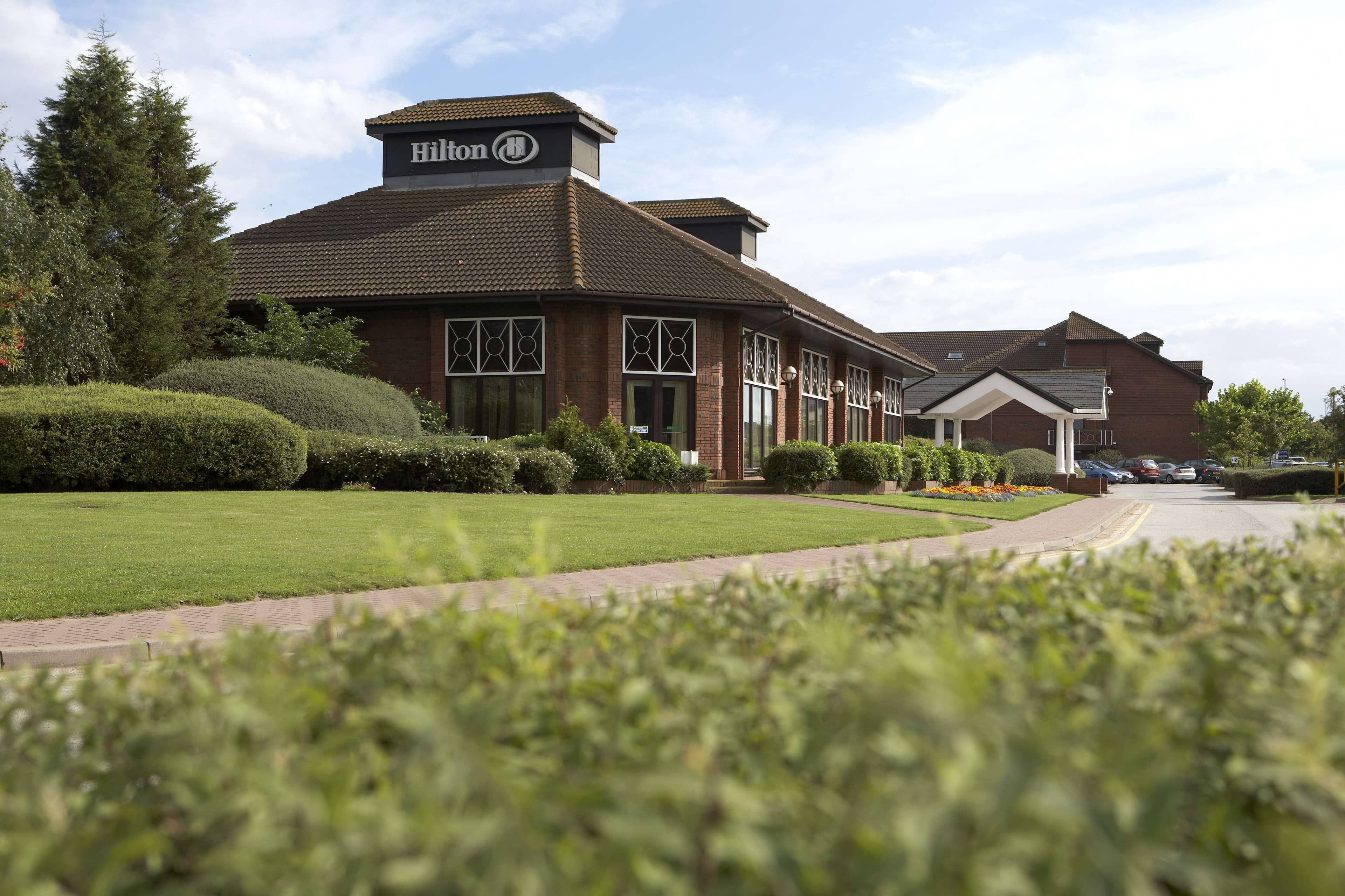 Exterior of Hilton East Midlands Airport hotel with manicured lawns and hedging in the foreground.